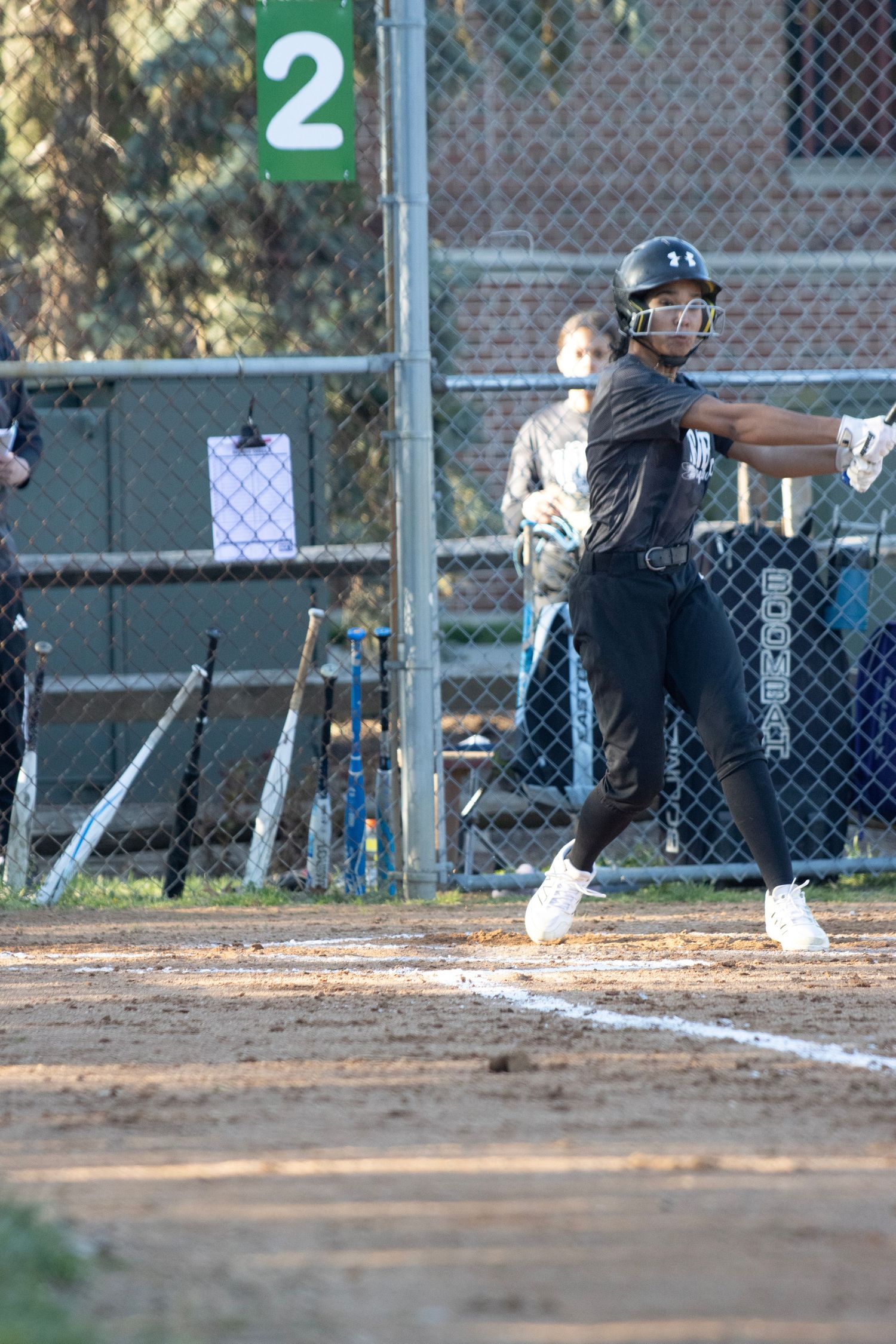 A softball player is standing at the home plate, right after hitting the ball.
