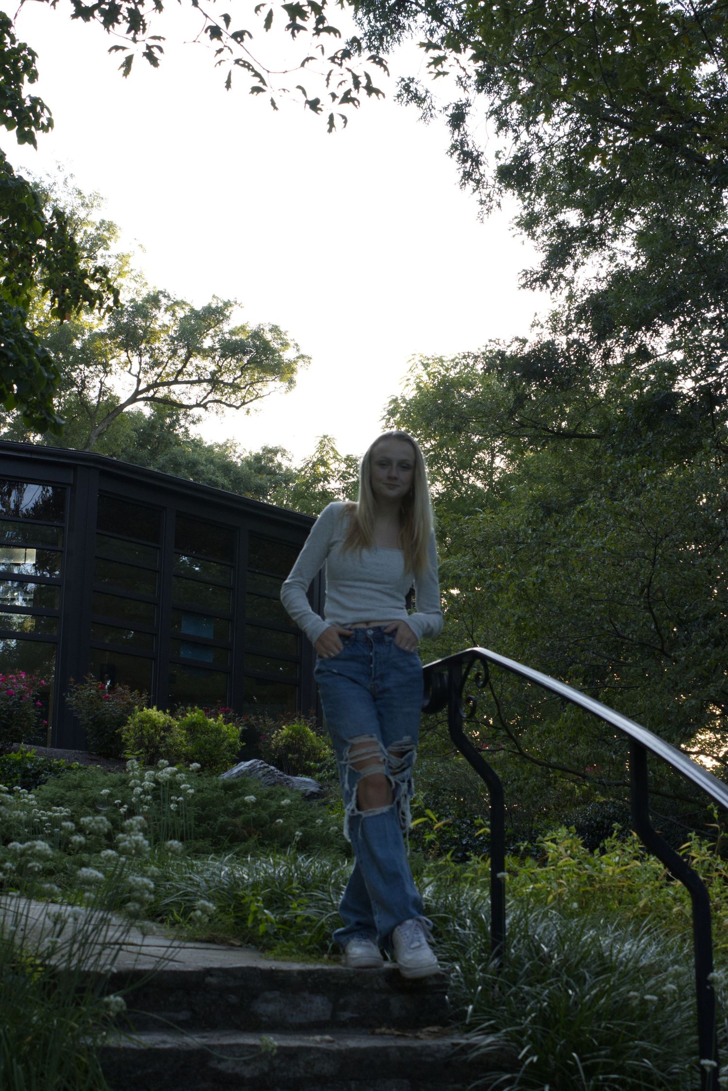 A young woman, standing on a set of stairs, is gazing directly at the camera.
