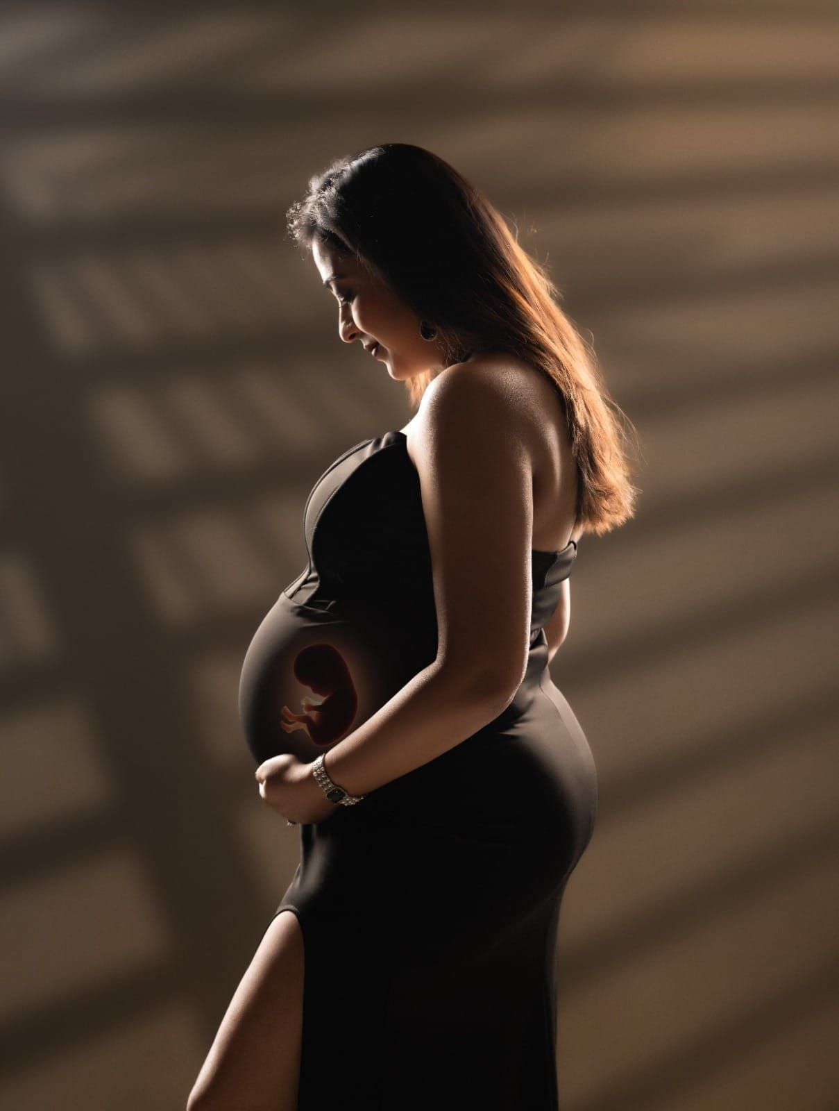 Silhouette maternity photo with sun rays showing pregnant woman holding her belly in black dress.