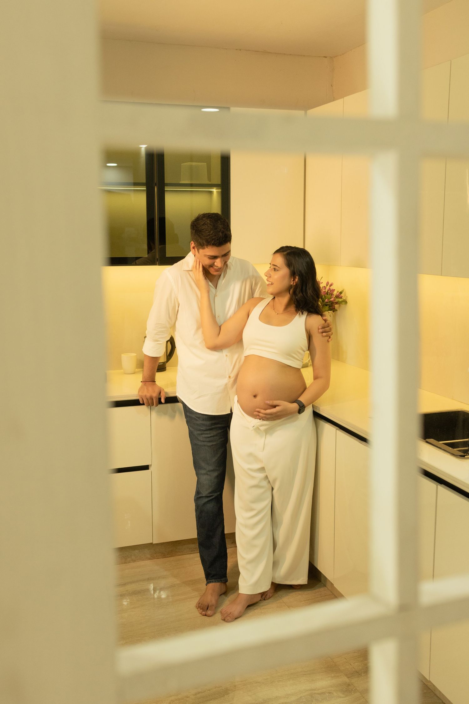 A couple embraces in an empty room with white columns while posing for maternity photos having an elegant maternity photoshoot.