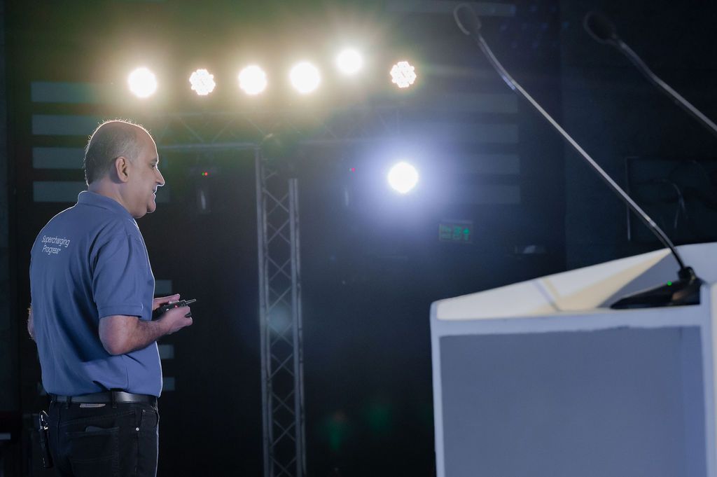 Stage lighting illuminates a dark conference or event space with silhouettes visible.