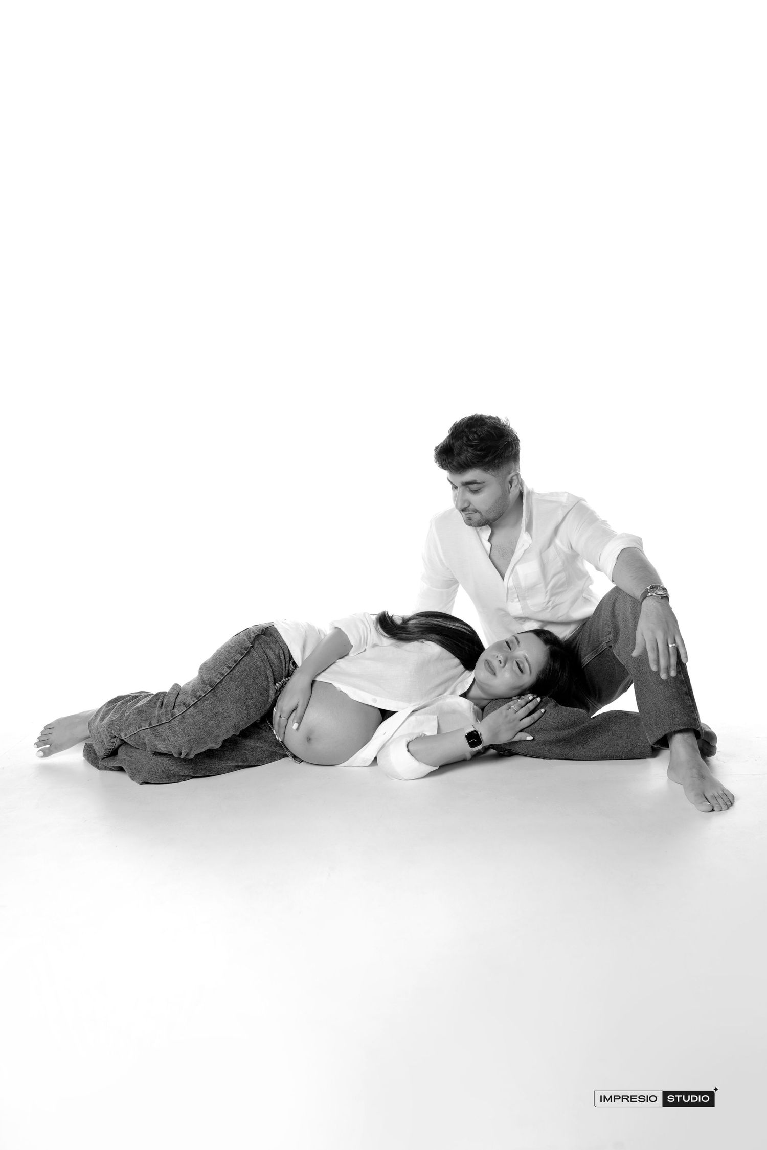 Black and white maternity photo of a couple sitting on floor, woman lying with head on man's lap.