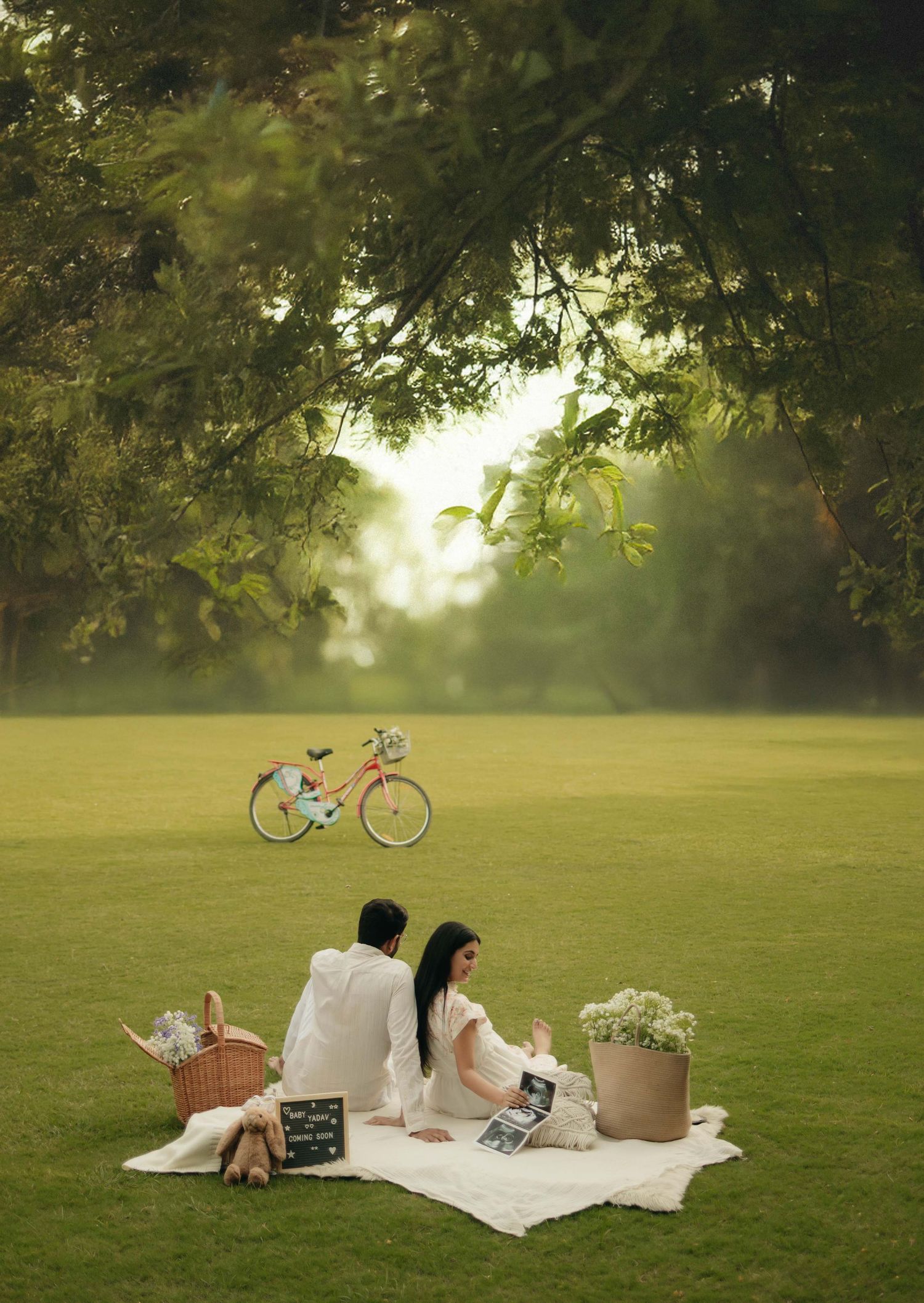 Couple enjoying a romantic picnic on a white blanket in a lush green park with a bicycle in the background.