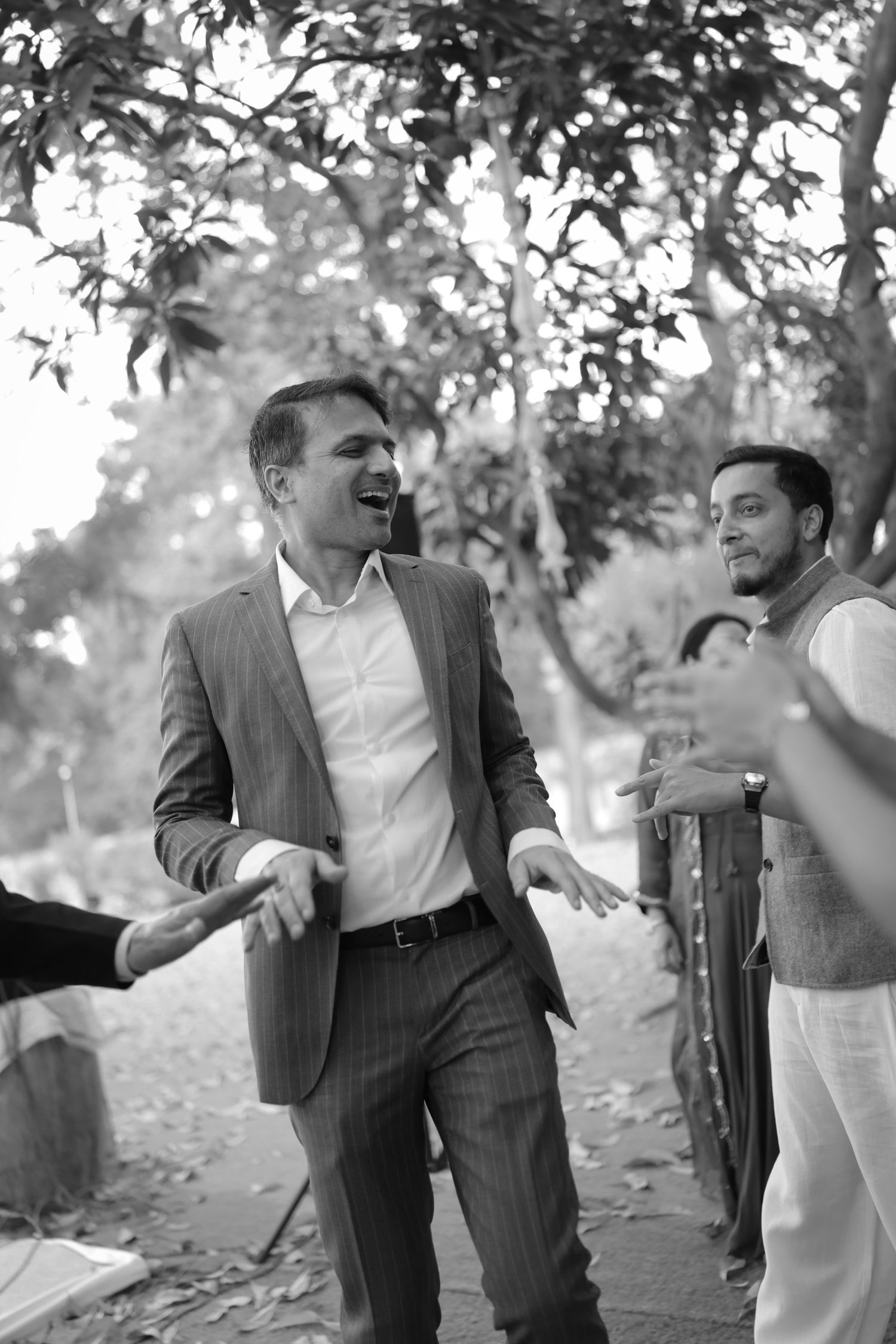 Black and white photo of men in suits laughing and dancing outdoors at a celebration event.