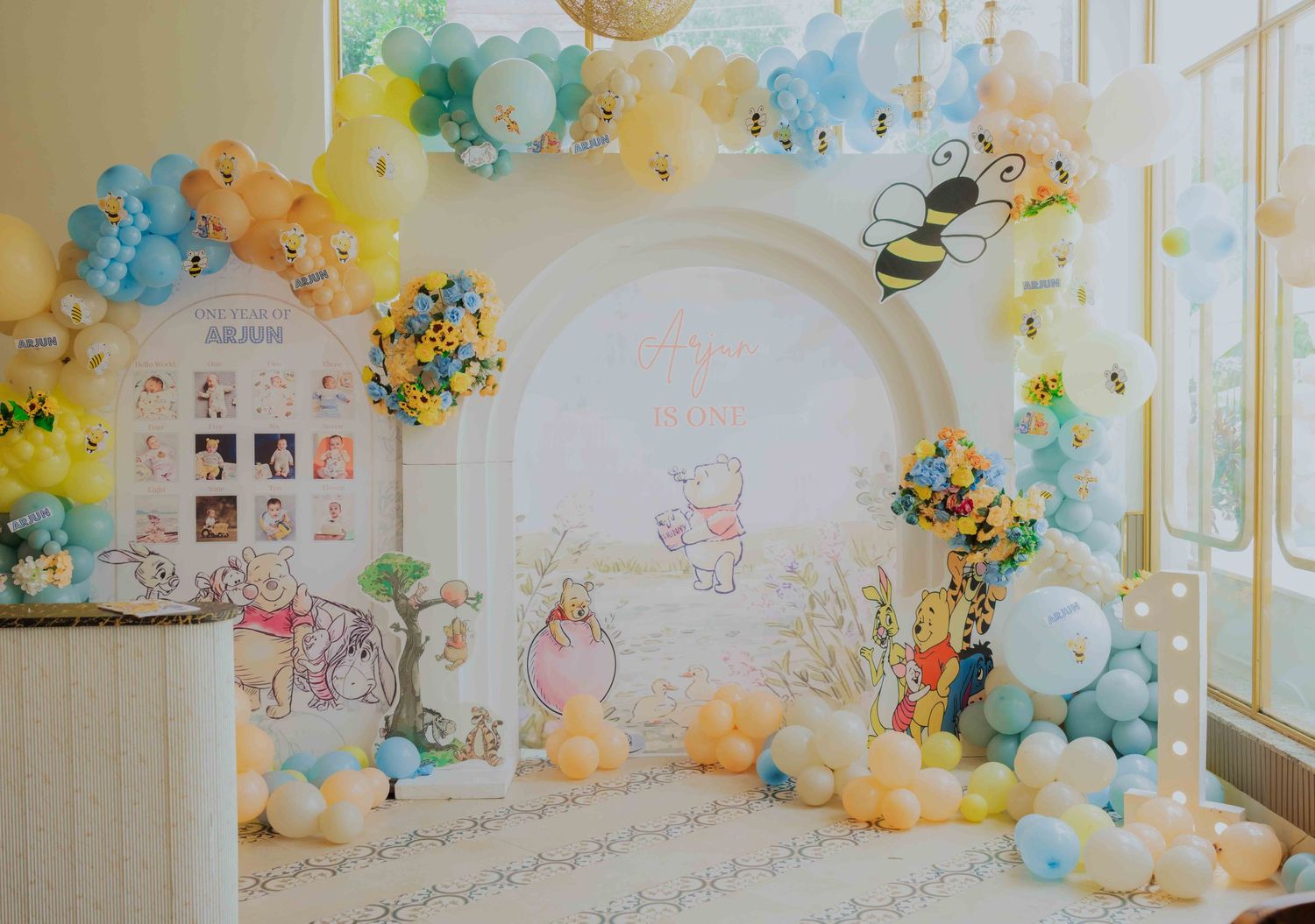 Winnie the Pooh baby shower backdrop with pastel balloon garland arch, honeybee accents, and circular photo display.