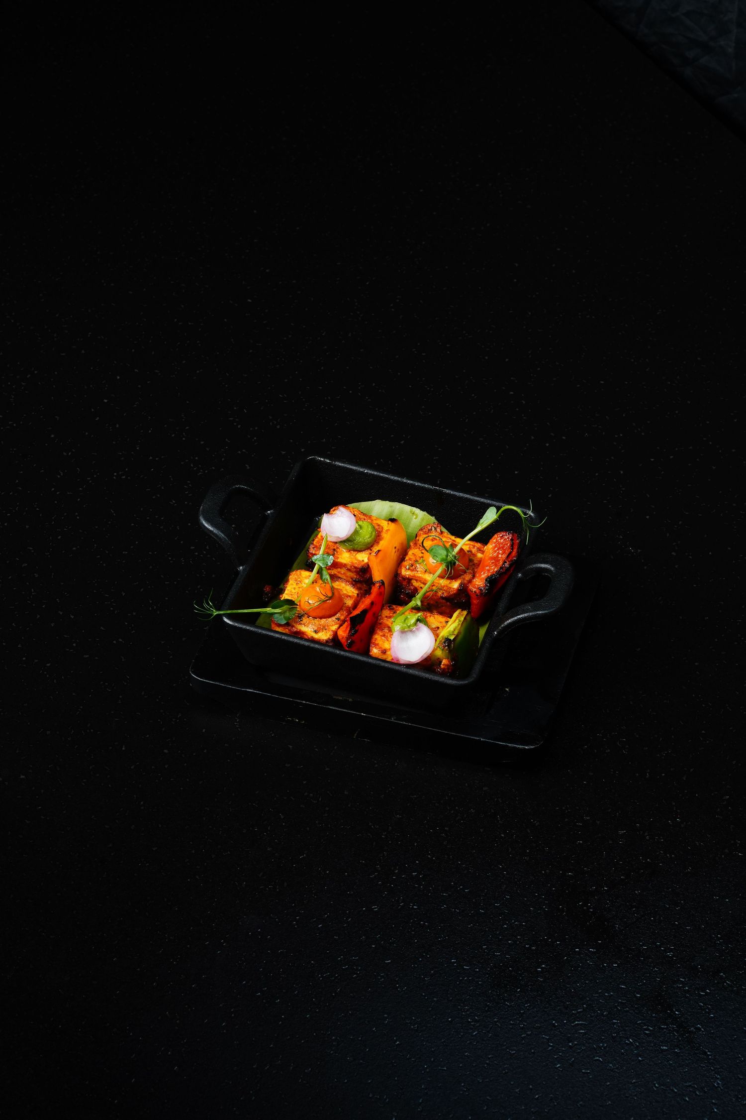 Colorful appetizer dish with garnishes served on black rectangular plate in moody lighting.