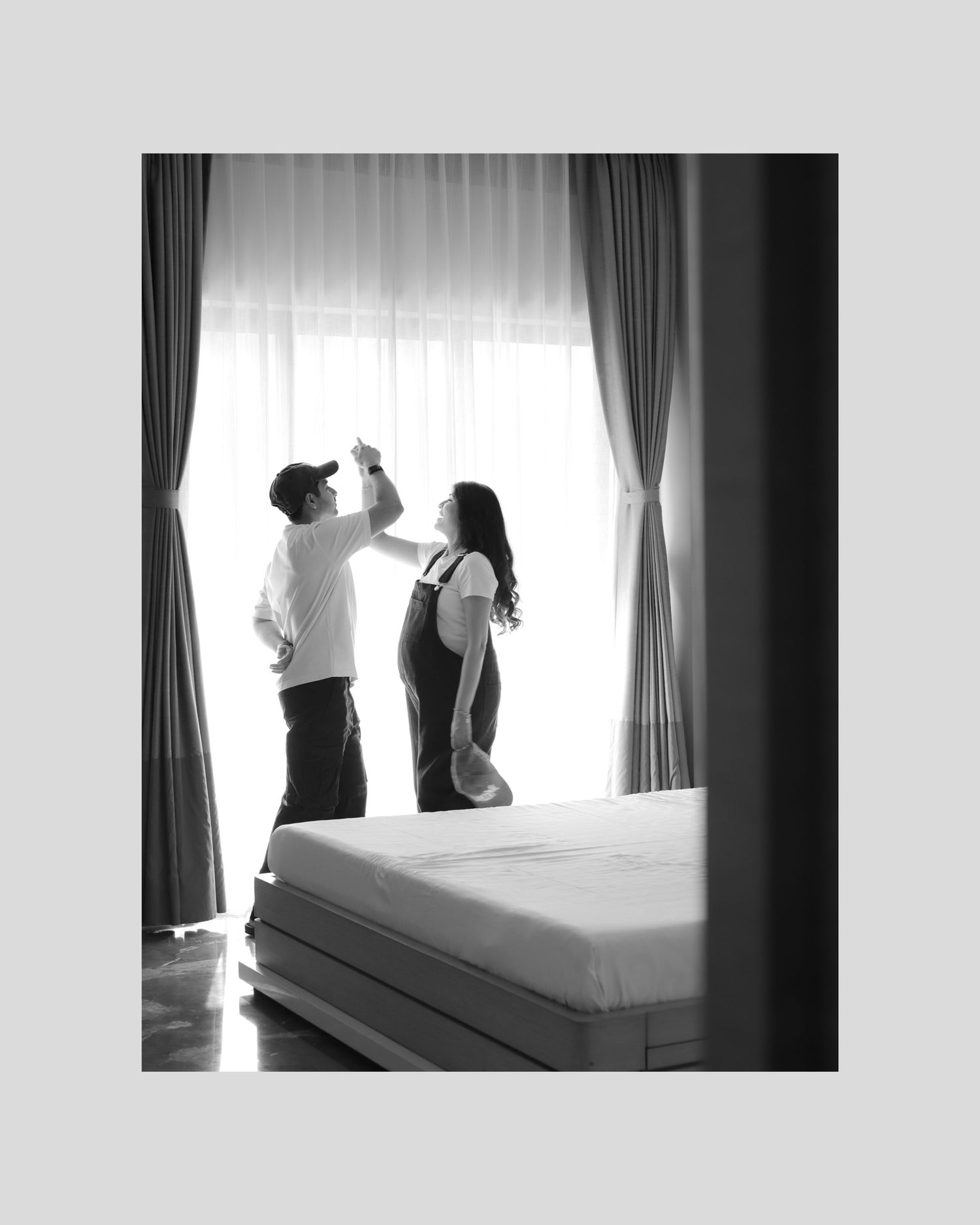 Two silhouettes stand together against a bright window in a bedroom, creating a romantic black and white composition.