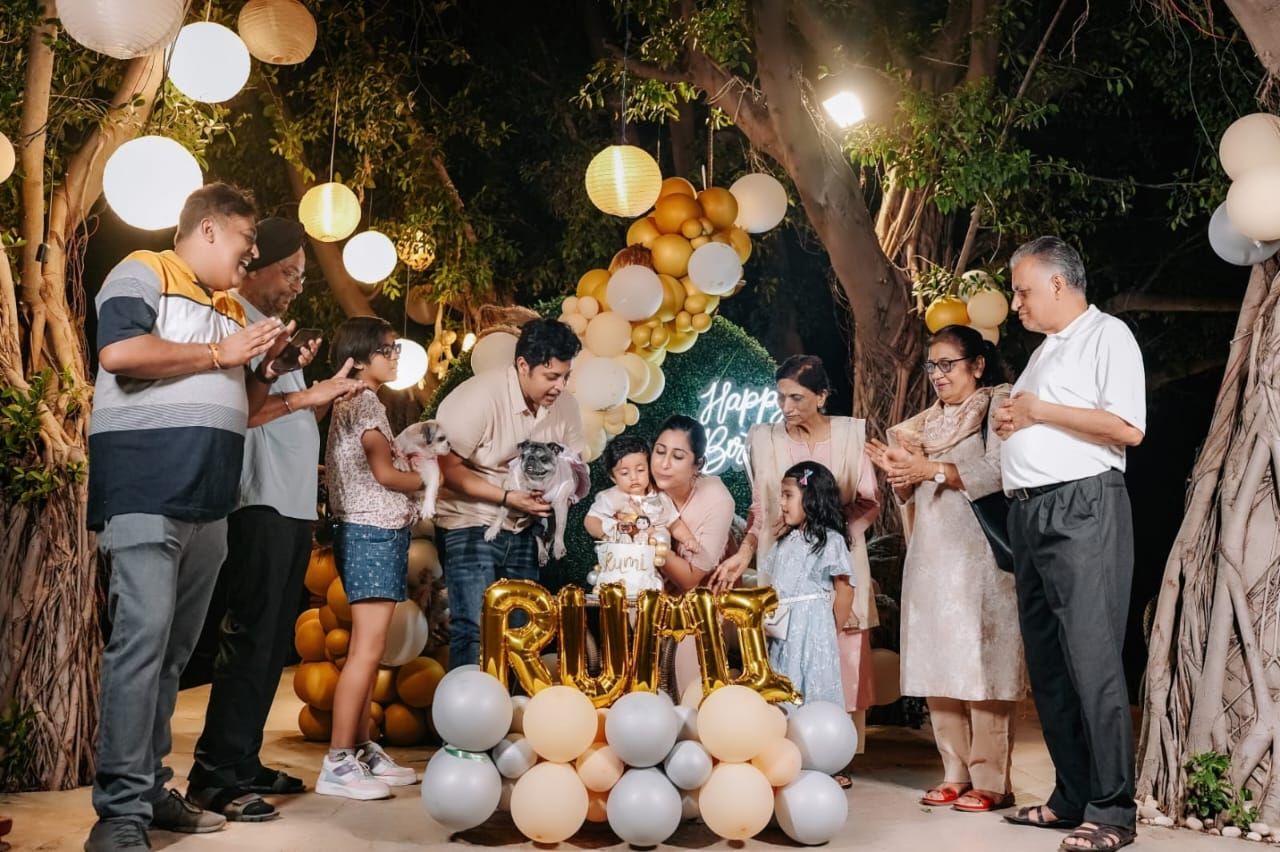 Family gathering around a birthday cake with gold and white balloon decorations at an outdoor night party.
