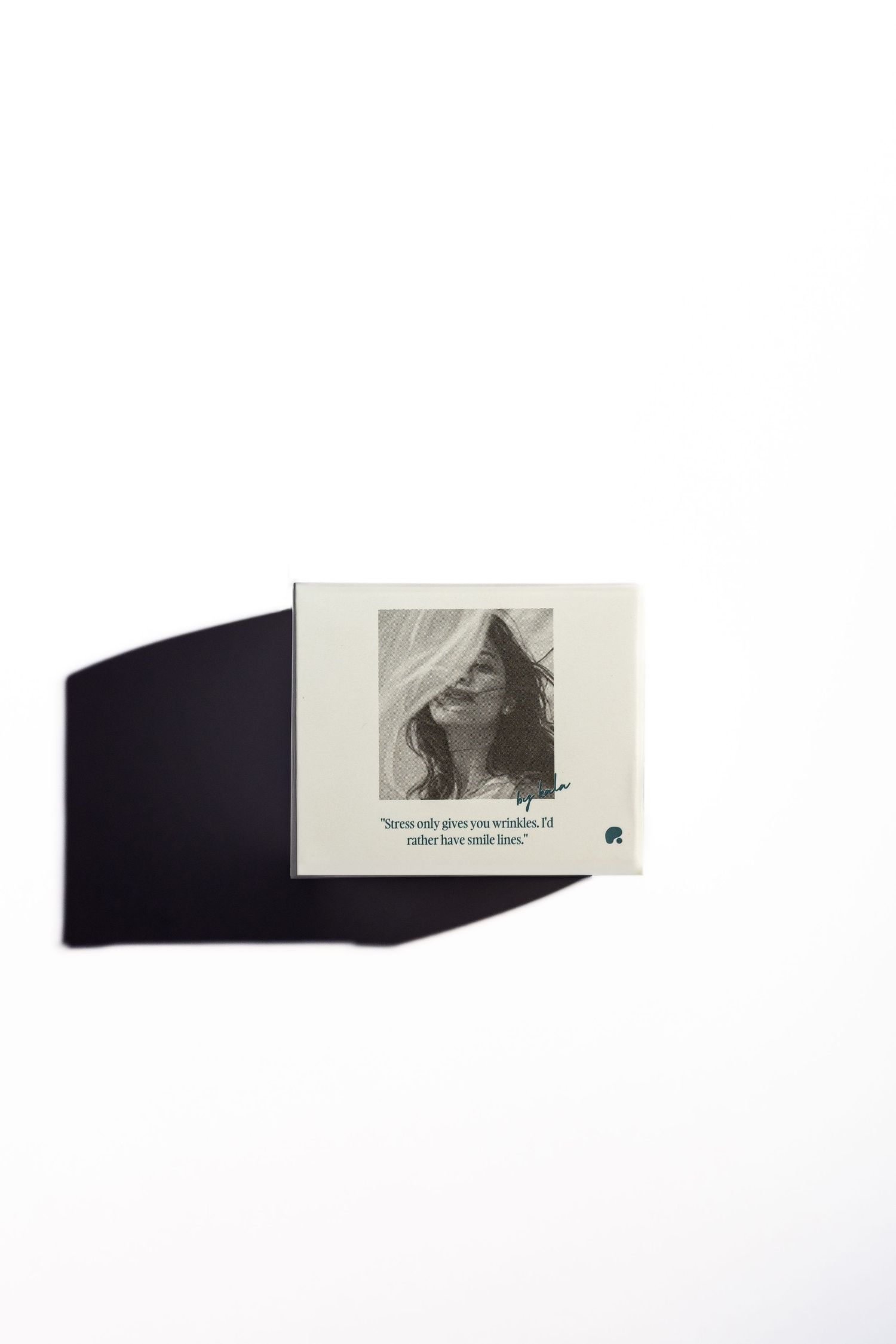 Cream-colored box with a black-and-white portrait of a woman with flowing hair and a quote about smile lines, casting a shadow on white.