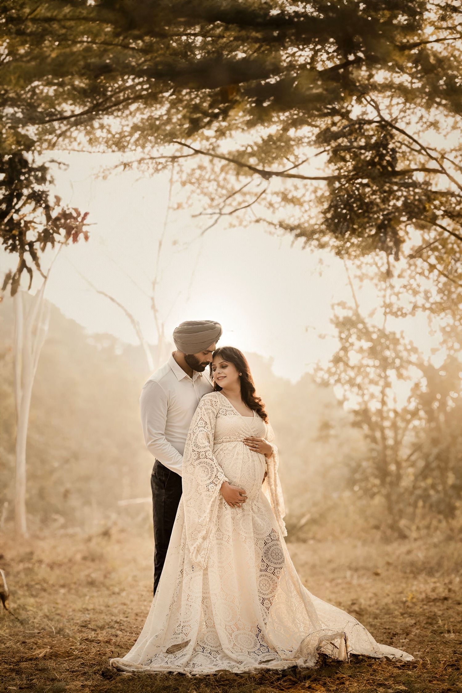 A couple in elegant white outfits share an intimate moment in a misty forest setting during golden hour.