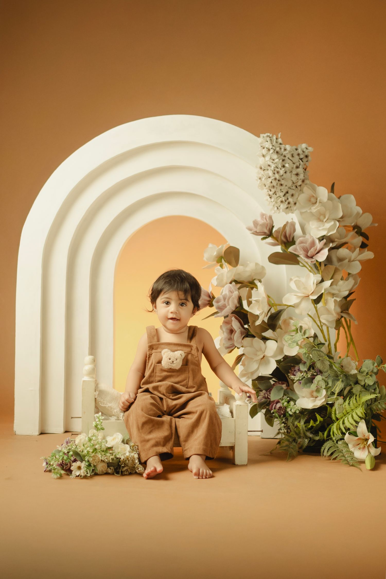 Minimalist studio setup with curved white arches and floral decorations against a warm beige background.