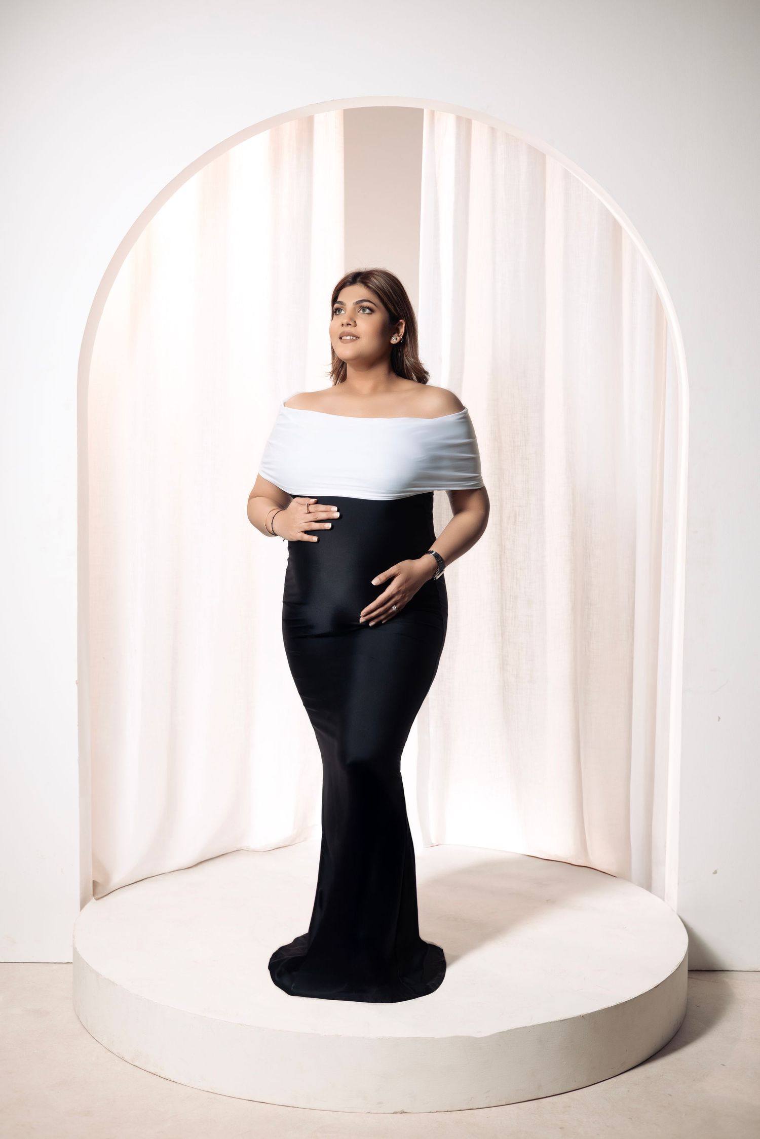 Elegant maternity photo of an expectant mother in a black and white gown on a circular platform.