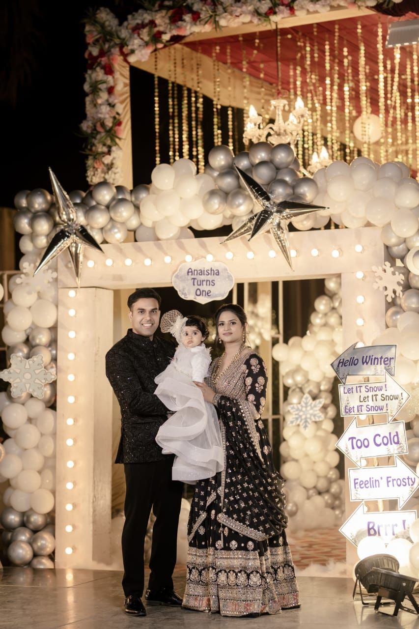 Family posing at a winter-themed first birthday party with balloon arch, star decorations, and festive signage.