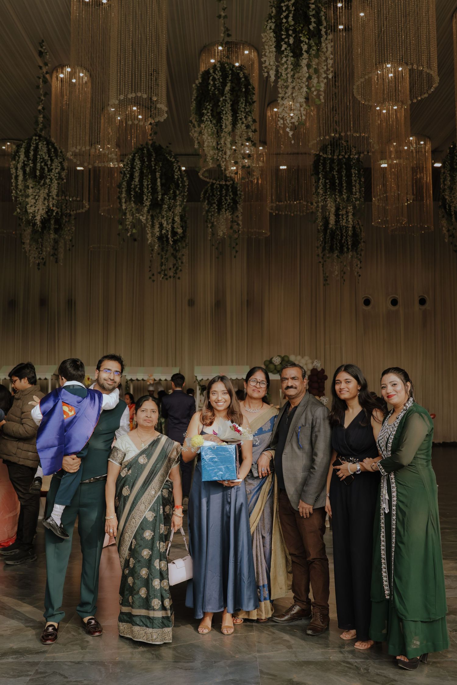 Group of elegantly dressed guests posing together at an Indian wedding reception with hanging floral decor.