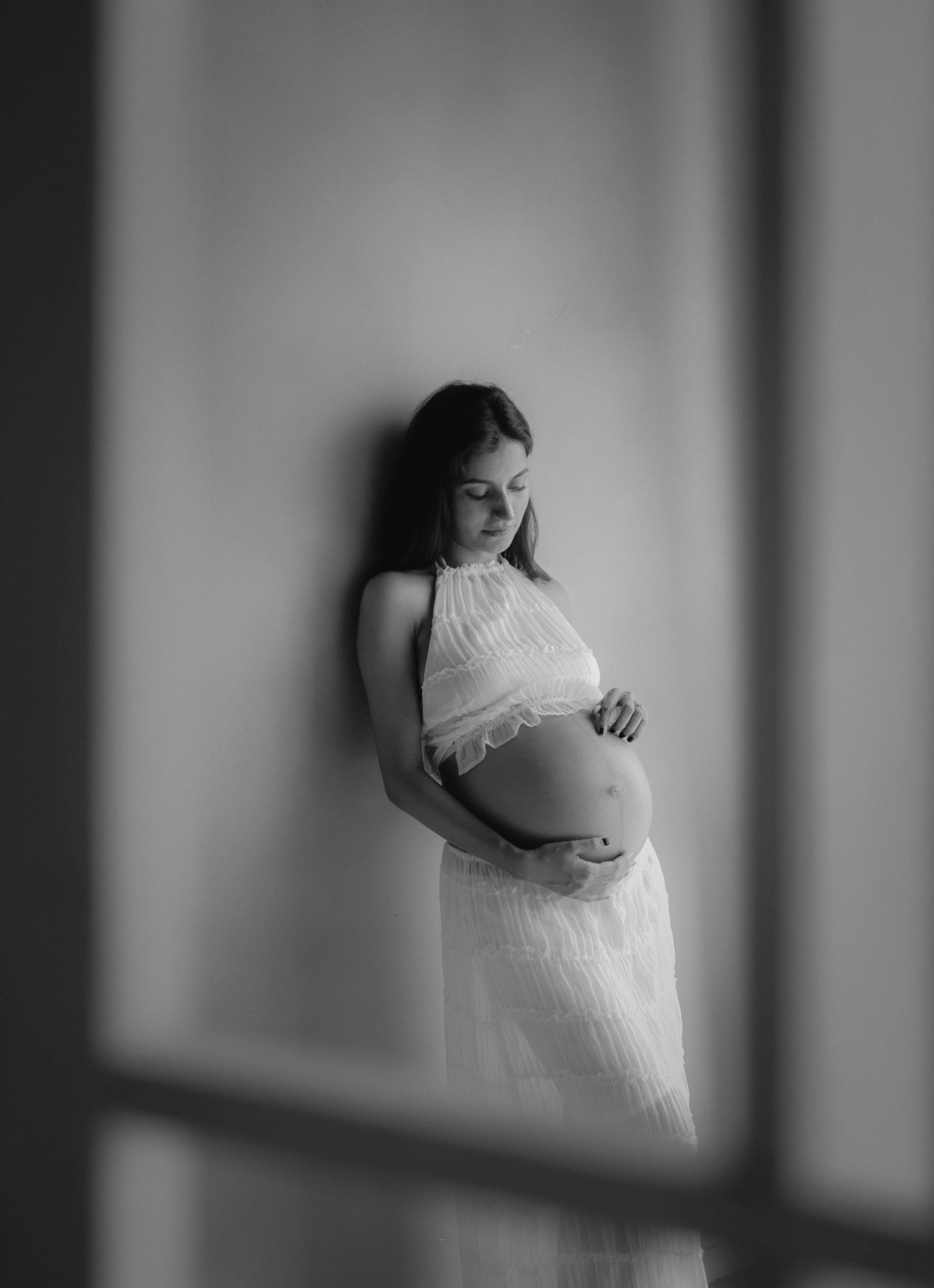 Black and white artistic maternity photo series showing a pregnant woman in white dress against dramatic lighting.