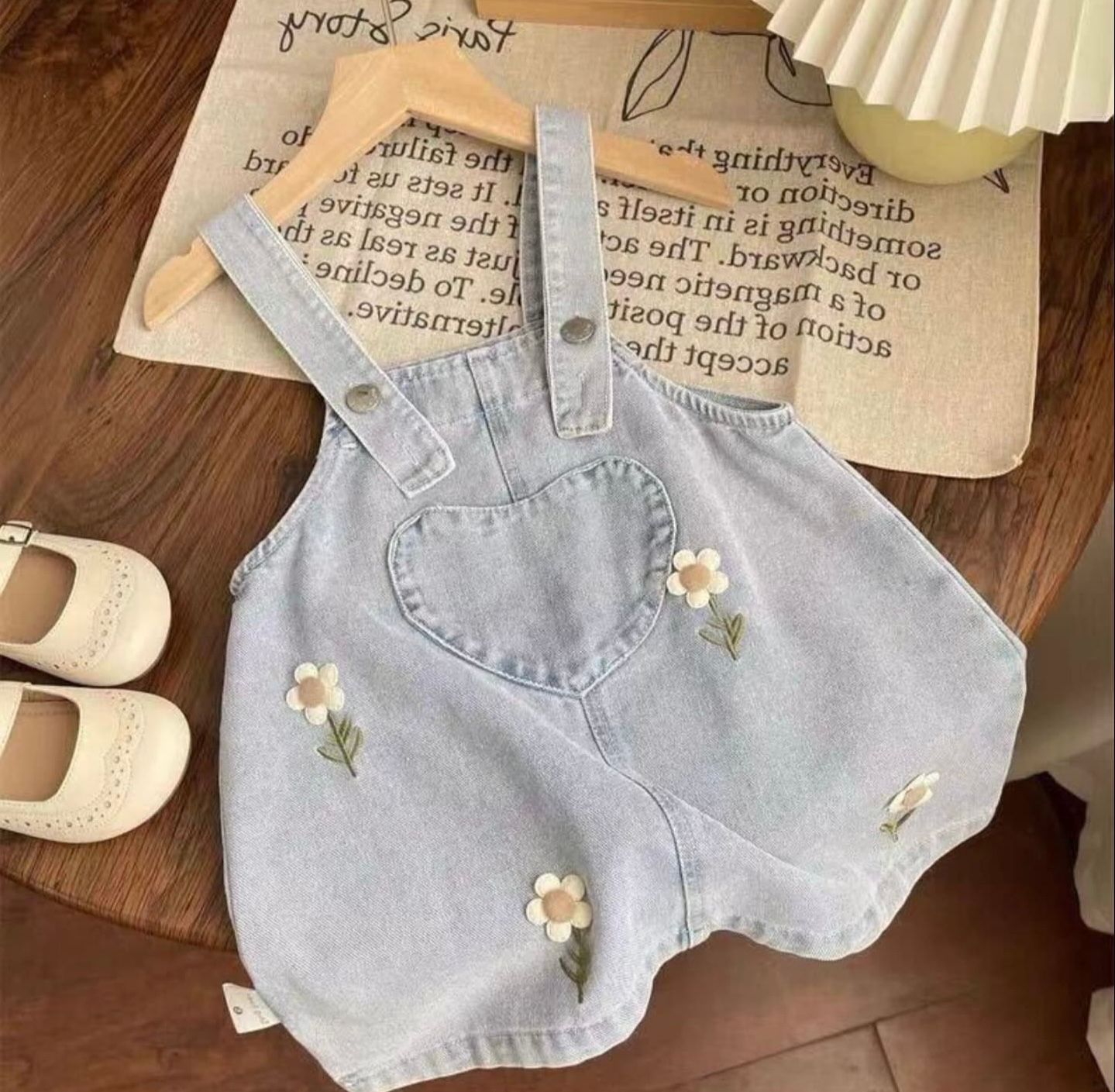 Denim shorts with small embroidered daisy flowers on light wash fabric displayed on wooden surface.