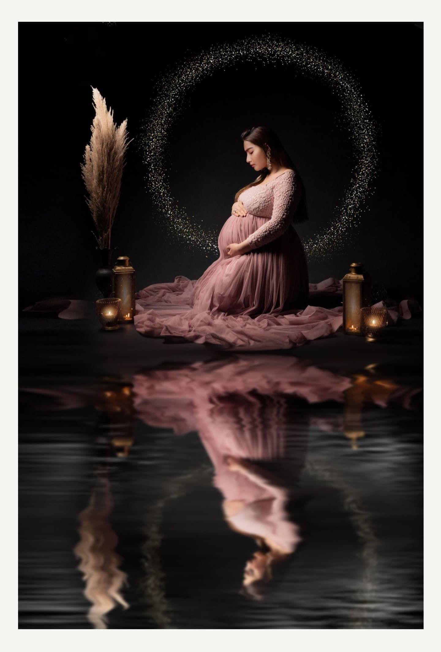 Artistic maternity portrait in pink dress with lanterns and reflections on dark water.