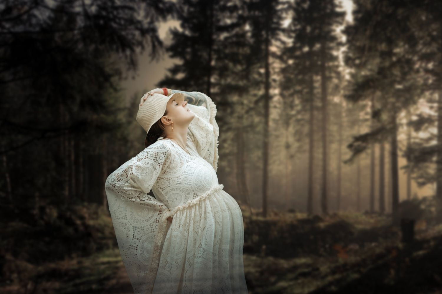 Pregnant woman in white lace dress and bonnet standing in misty forest, looking up gracefully.