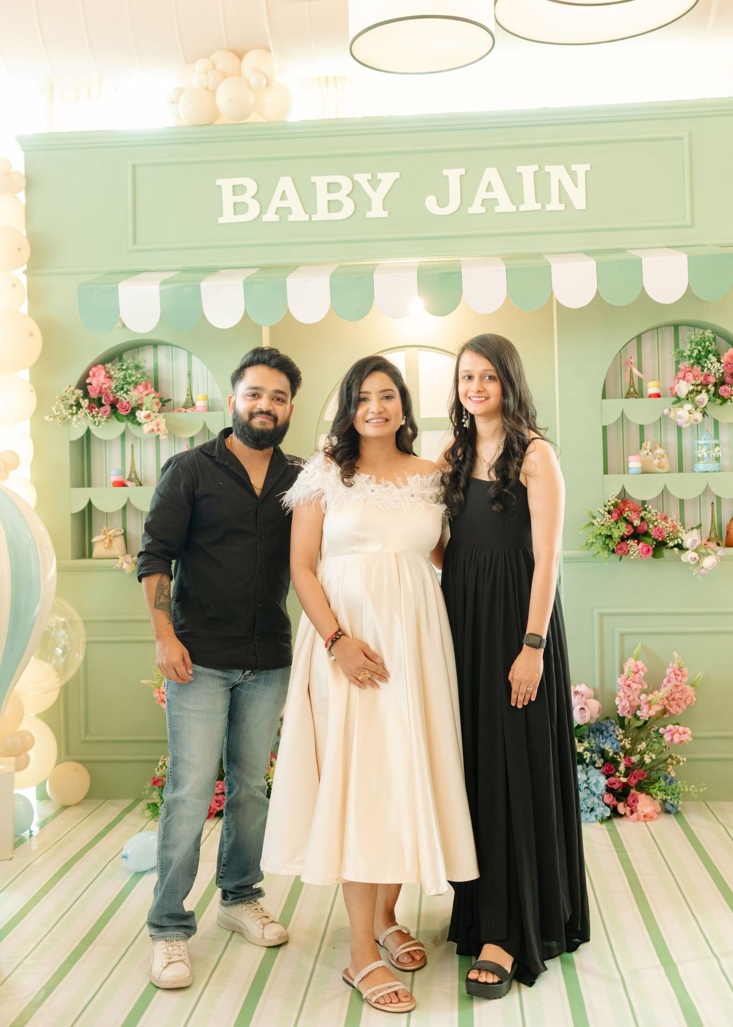 Three guests pose at a Baby Jain baby shower celebration in front of a mint green decorative backdrop with flowers.