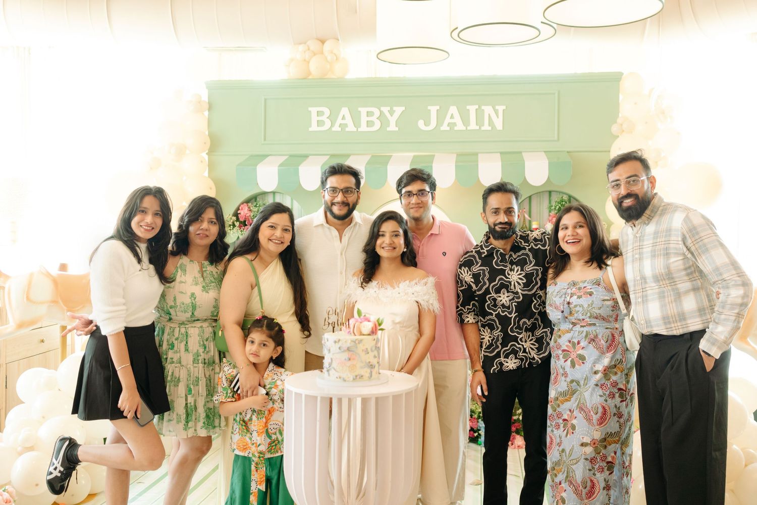Group of friends and family celebrating a Baby Jain baby shower with a cake and balloon decorations.