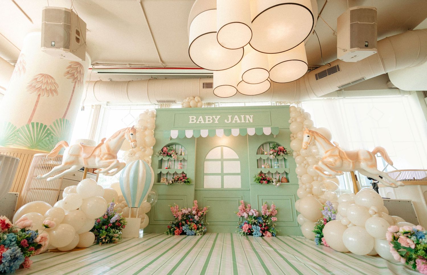 Elegant baby shower backdrop with mint green decor, white balloons, floral arrangements, and Baby Jain signage.