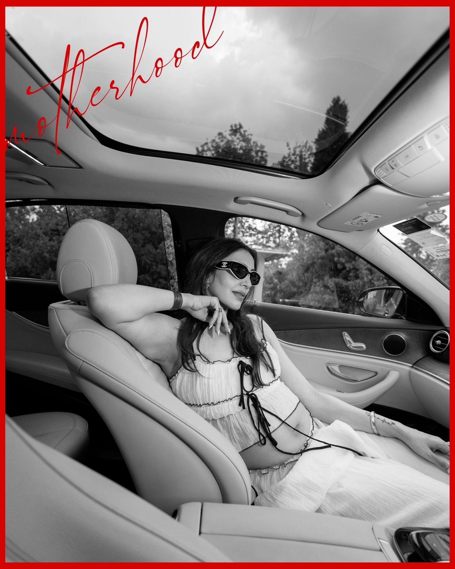 Black and white photo of a stylish woman in sunglasses relaxing in a luxury car with sunroof, captioned Motherhood.