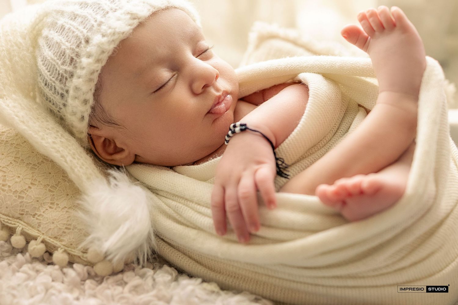 Peaceful newborn baby sleeping wrapped in cream knit blanket wearing white hat, professional newborn photography.
