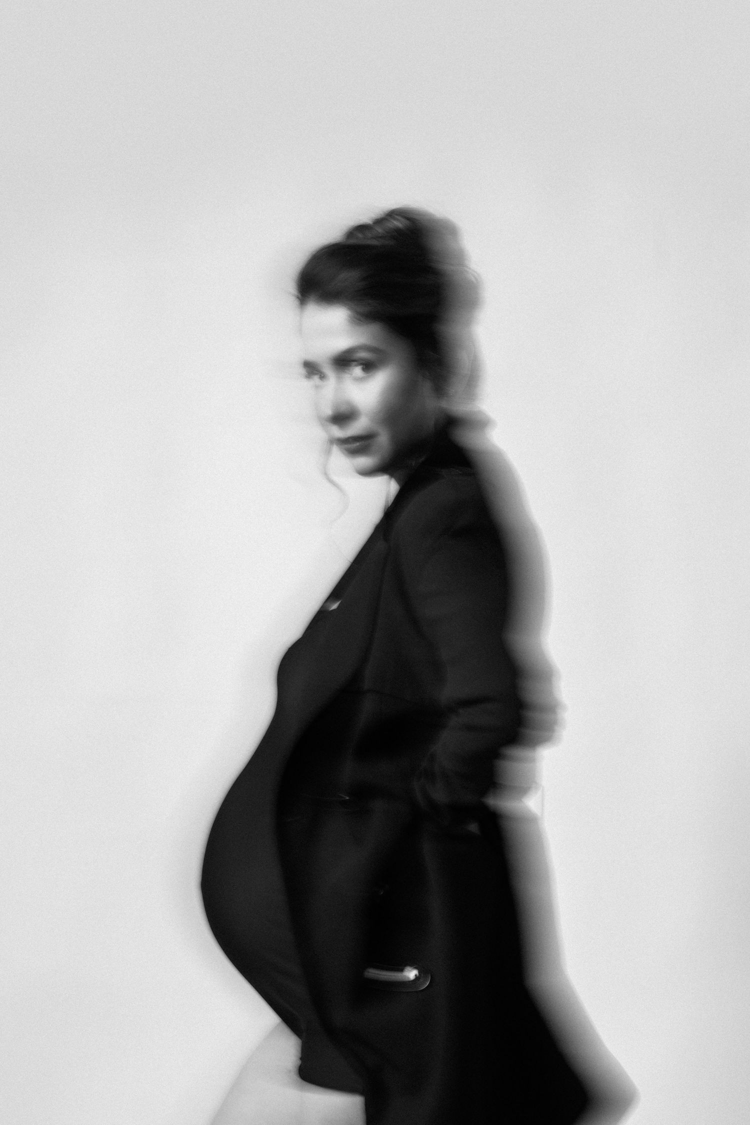 Black and white artistic portrait of an expectant woman in a suit jacket turning sideways showing her pregnancy silhouette.