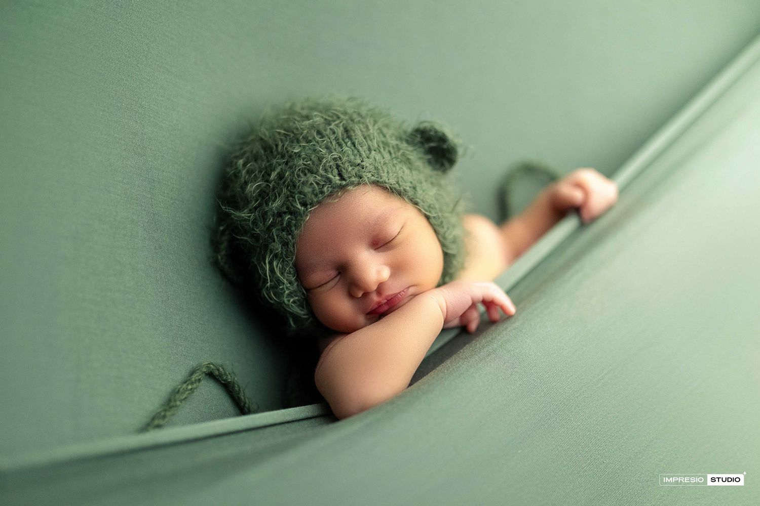 Newborn baby sleeping peacefully wrapped in green fabric wearing a cozy knit green bear hat.