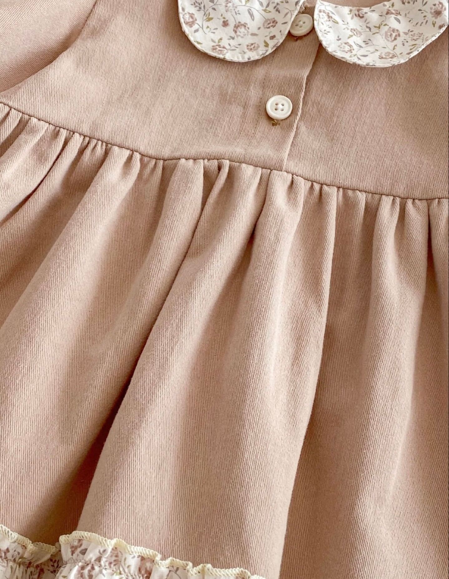Close-up of a beige linen dress with gathered detail and white button at the bodice.