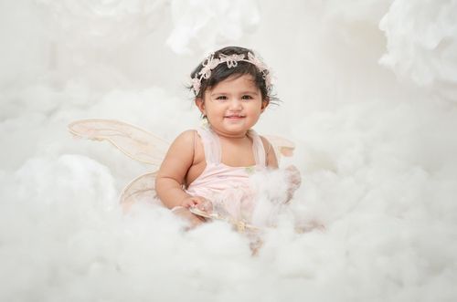 Ethereal portrait of small child with fairy wings lying on soft white clouds.