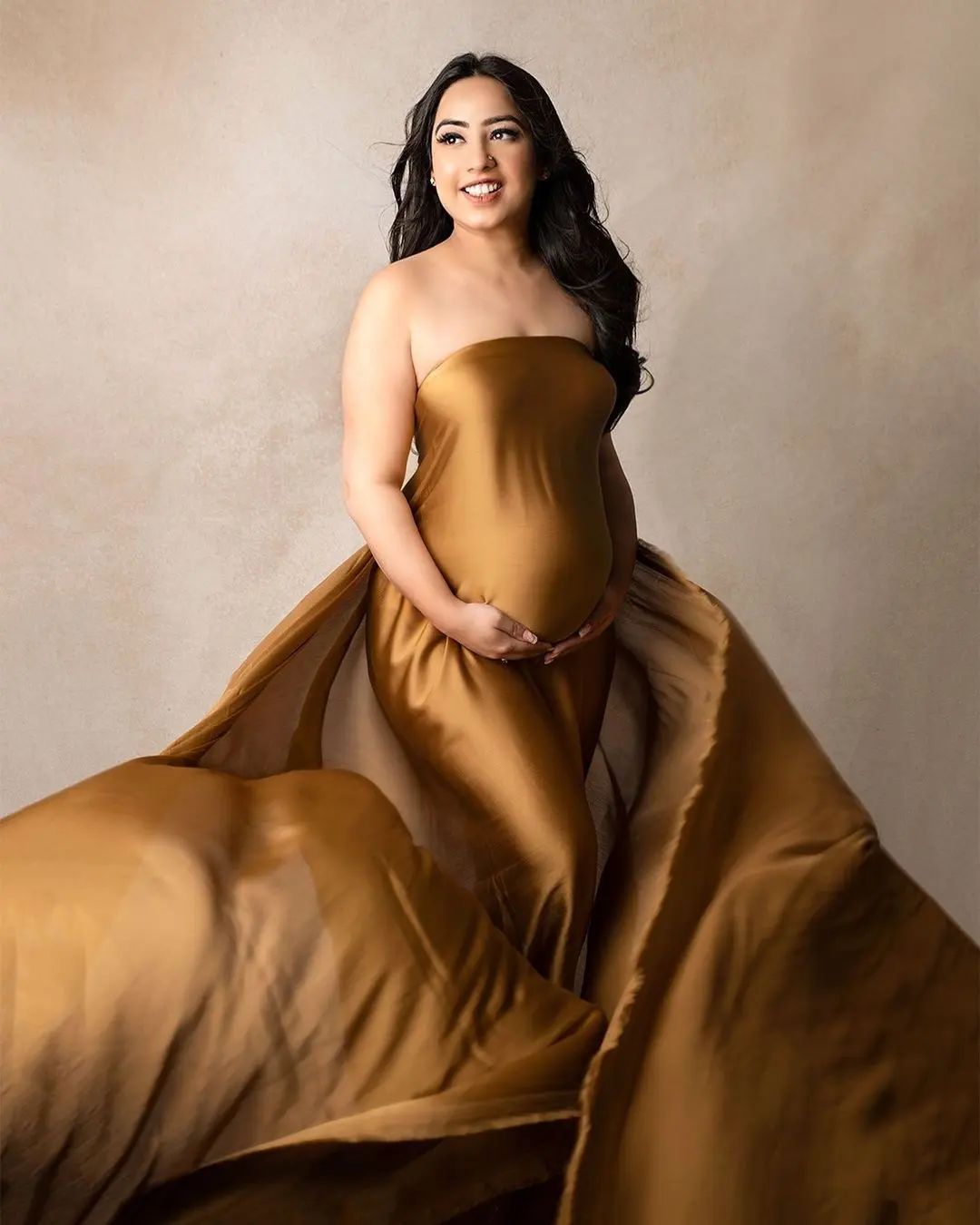 An elegant maternity photoshoot featuring a flowing brown fabric against a neutral backdrop.