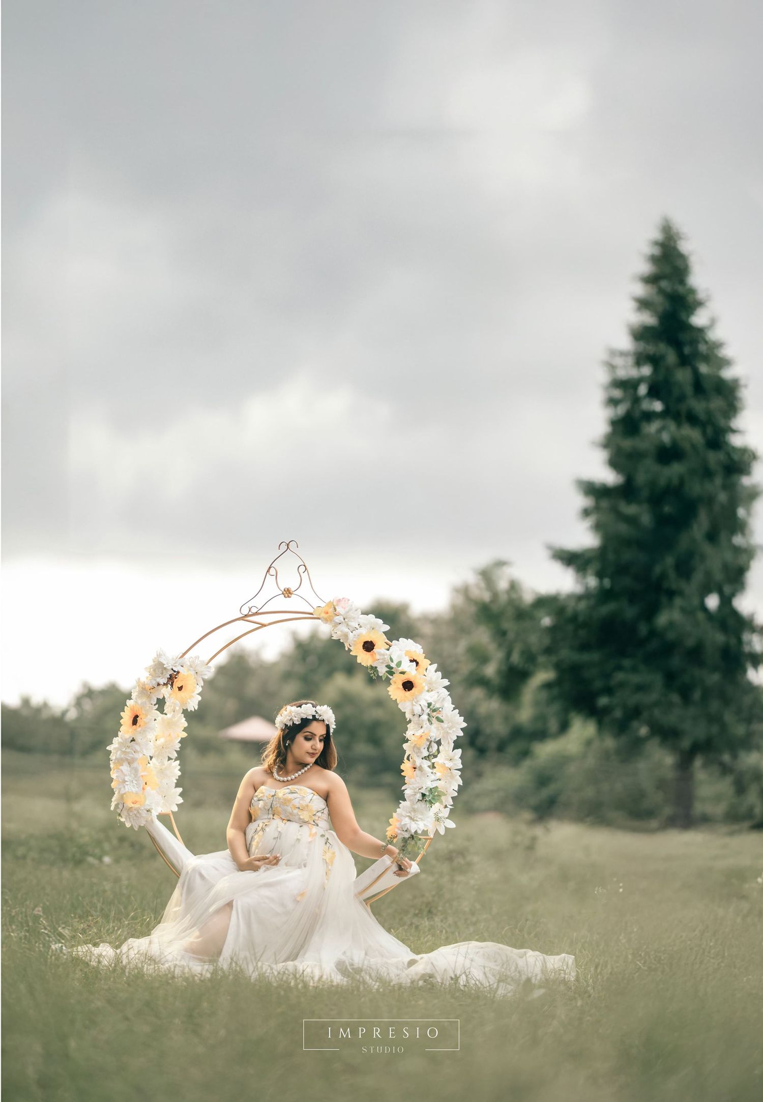 Dreamy outdoor maternity photo with floral wreaths in meadow setting.