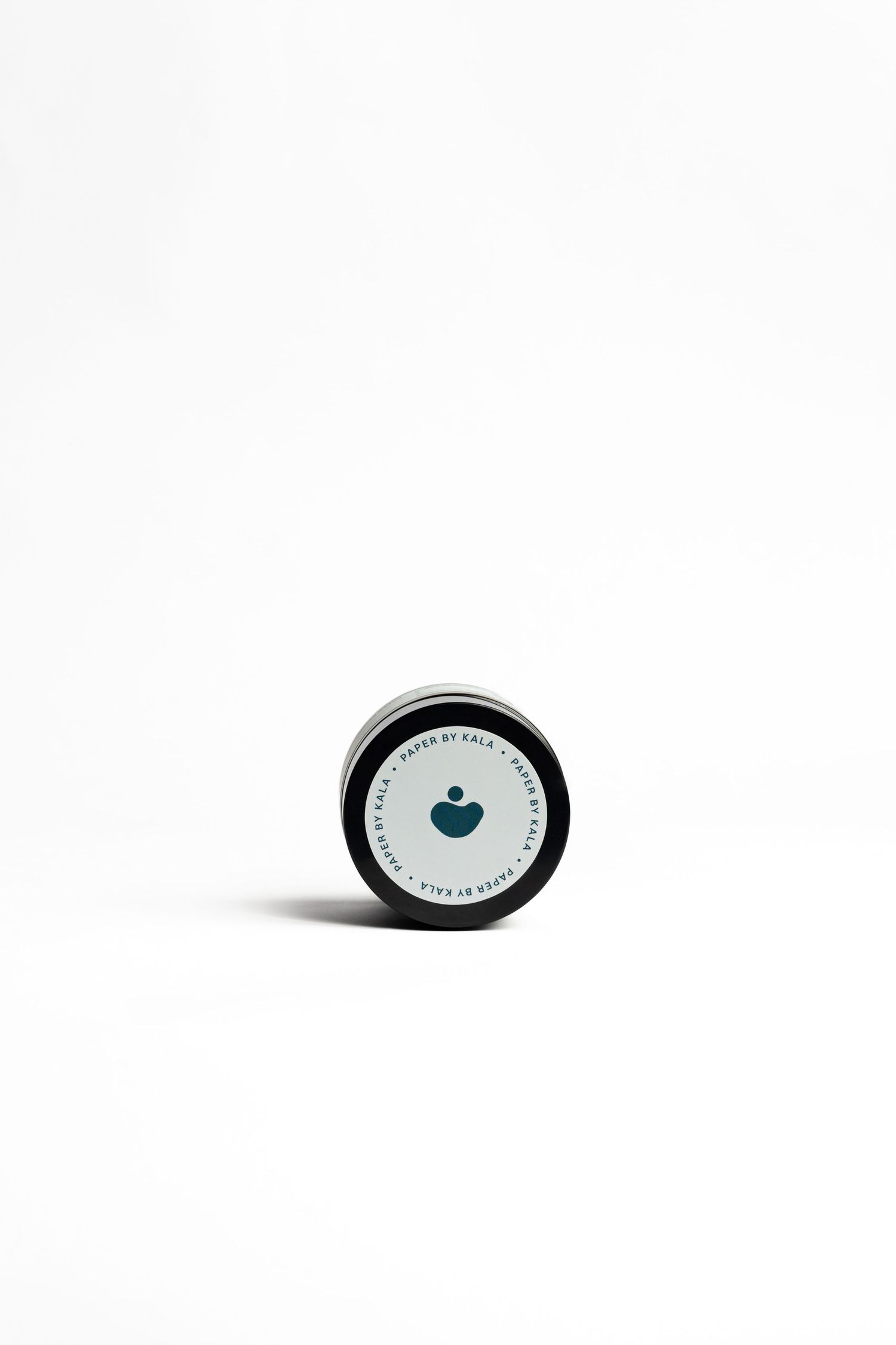 Small round black tin with a white lid featuring a teal heart and person icon and circular text reading Made by Kala.