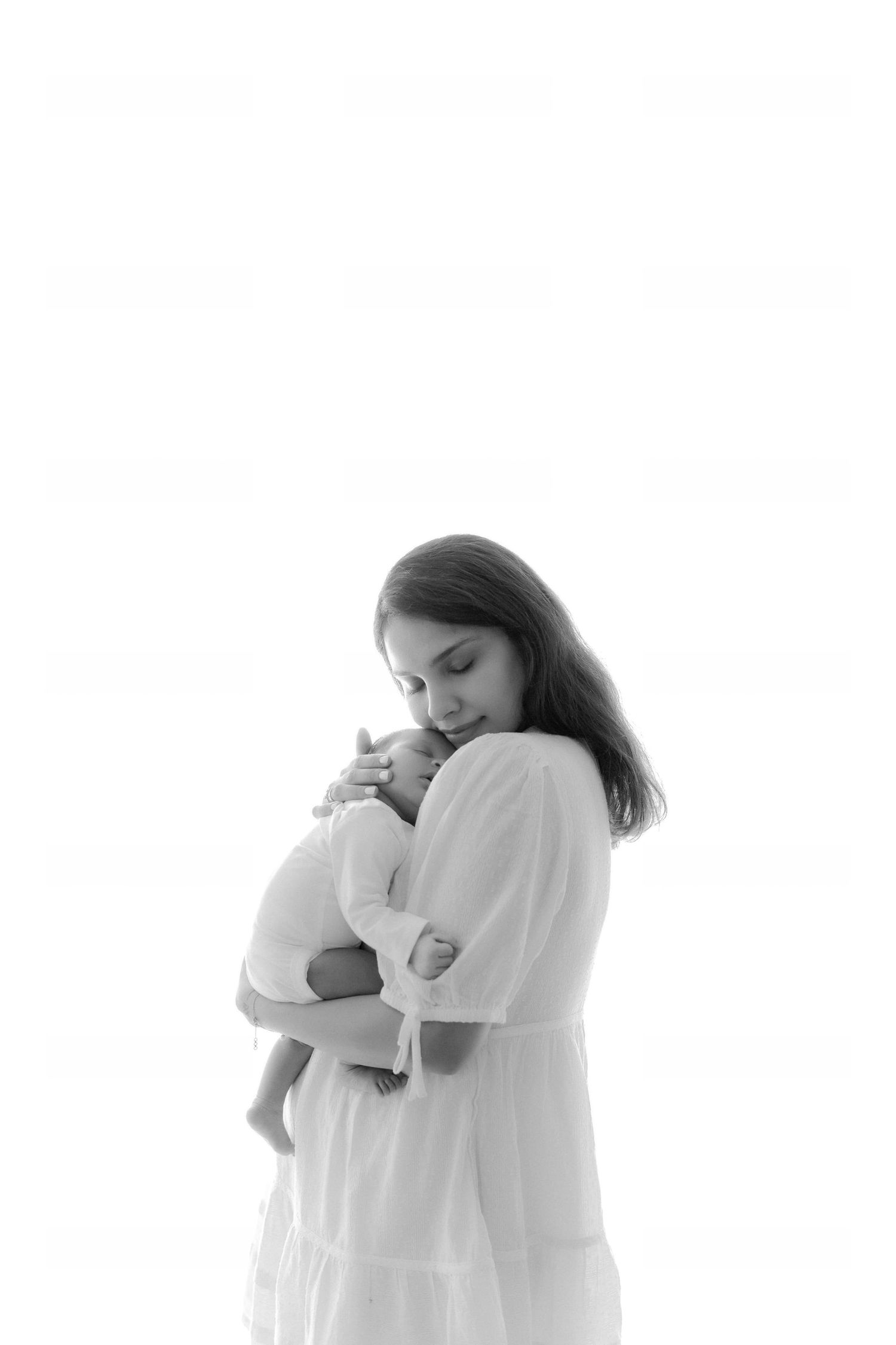 Black and white photo of mother in white dress tenderly holding and cradling her newborn baby.