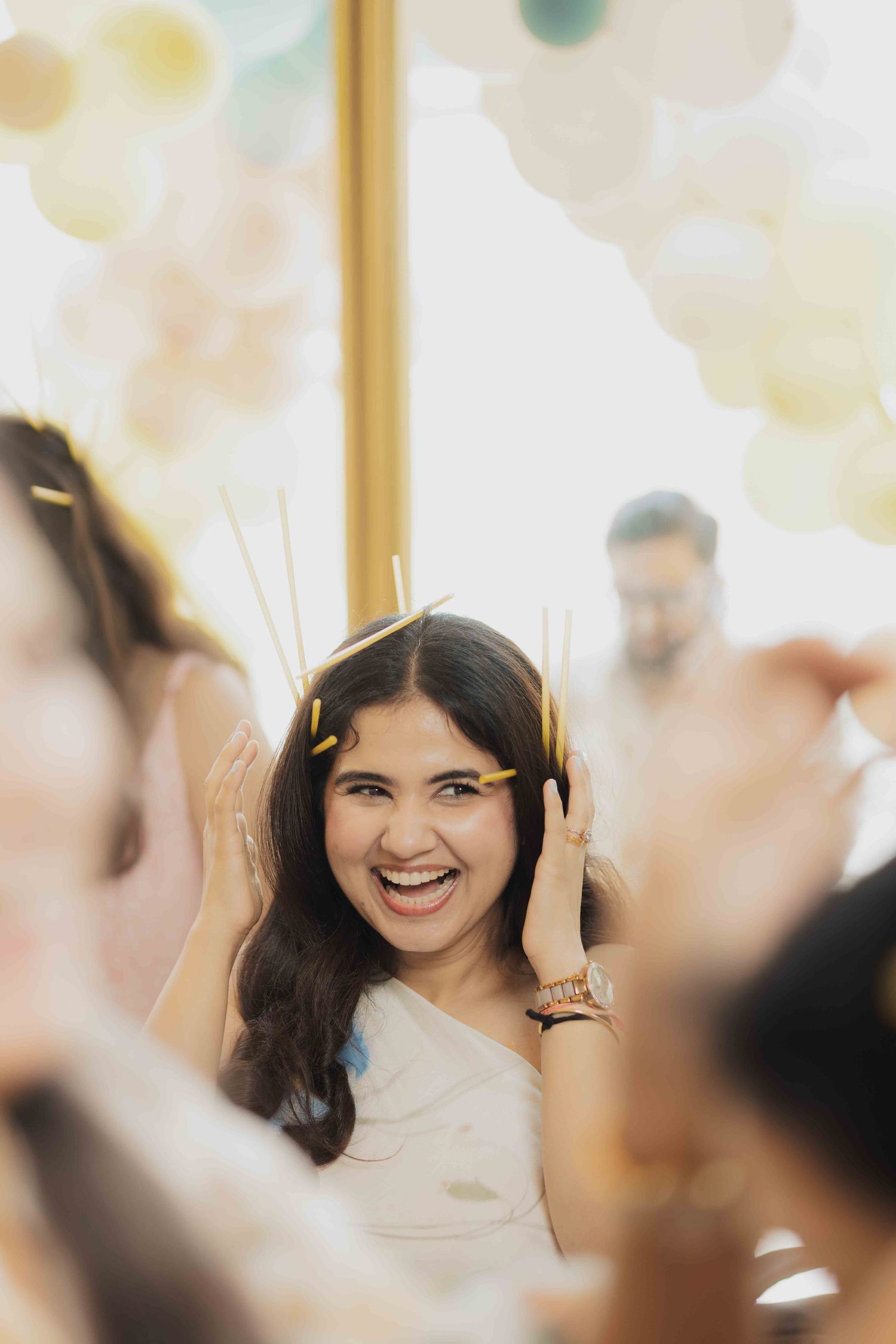 A joyful young woman laughs at a festive party, surrounded by colorful balloons and confetti in her hair.