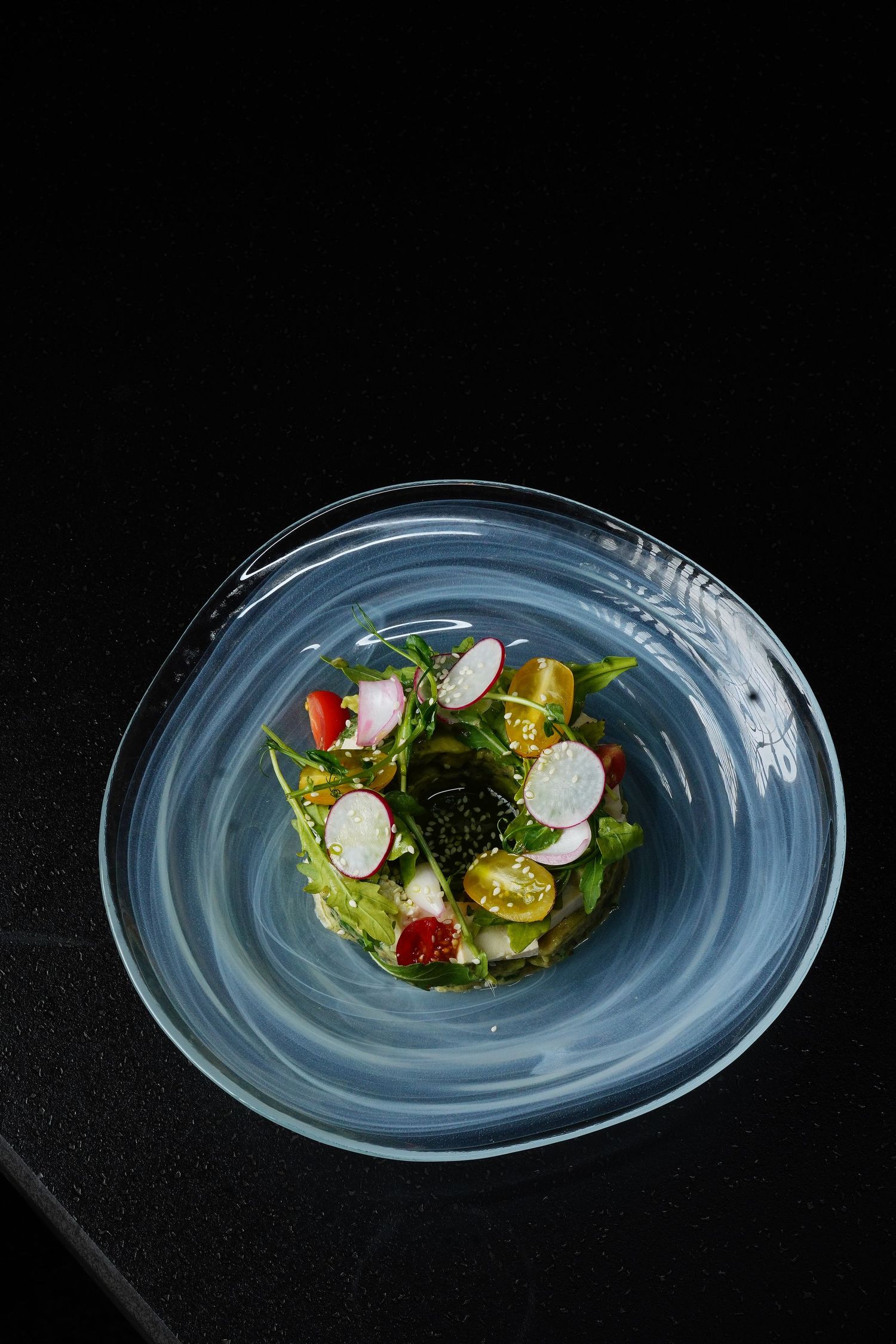Fresh salad with sliced radishes, greens, and citrus served on a swirled blue ceramic plate.