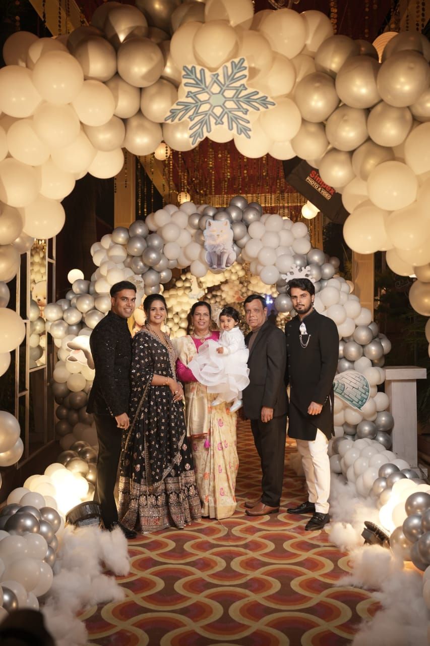 Family posing under elegant balloon arch with snowflake decor at Indian celebration event.