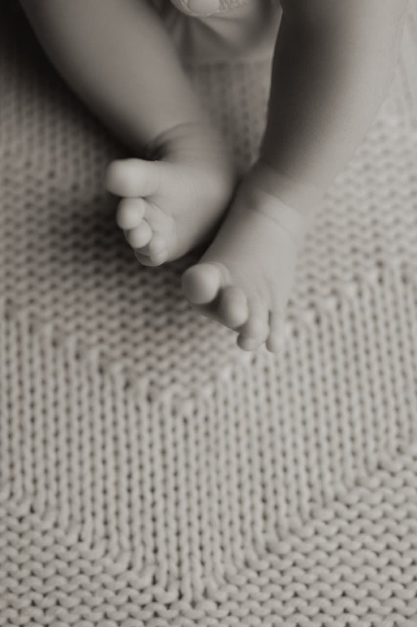 Black and white close-up photo of tiny newborn baby feet resting on a soft knitted blanket.