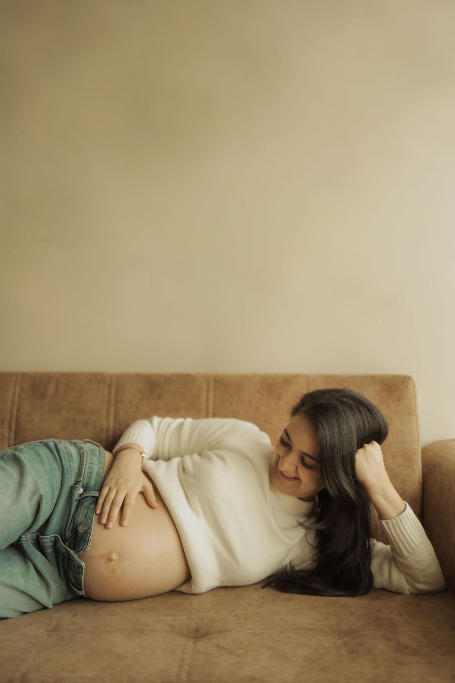 A series of connected photos showing a pregnant person lying on their side in a cream-colored artistic maternity portrait.