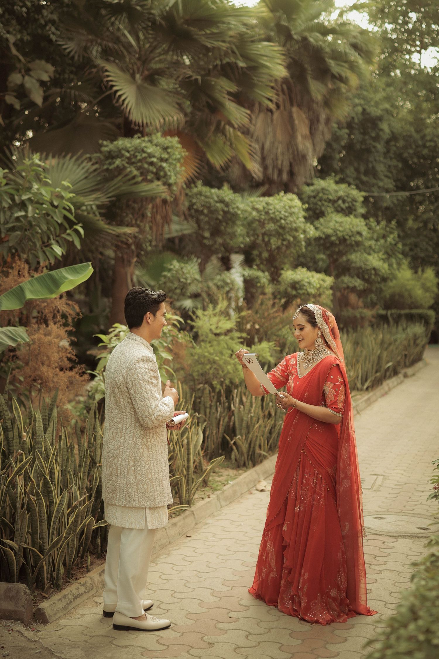 Indian couple in traditional wedding attire exchanging rings in a lush garden setting, bride in red lehenga.