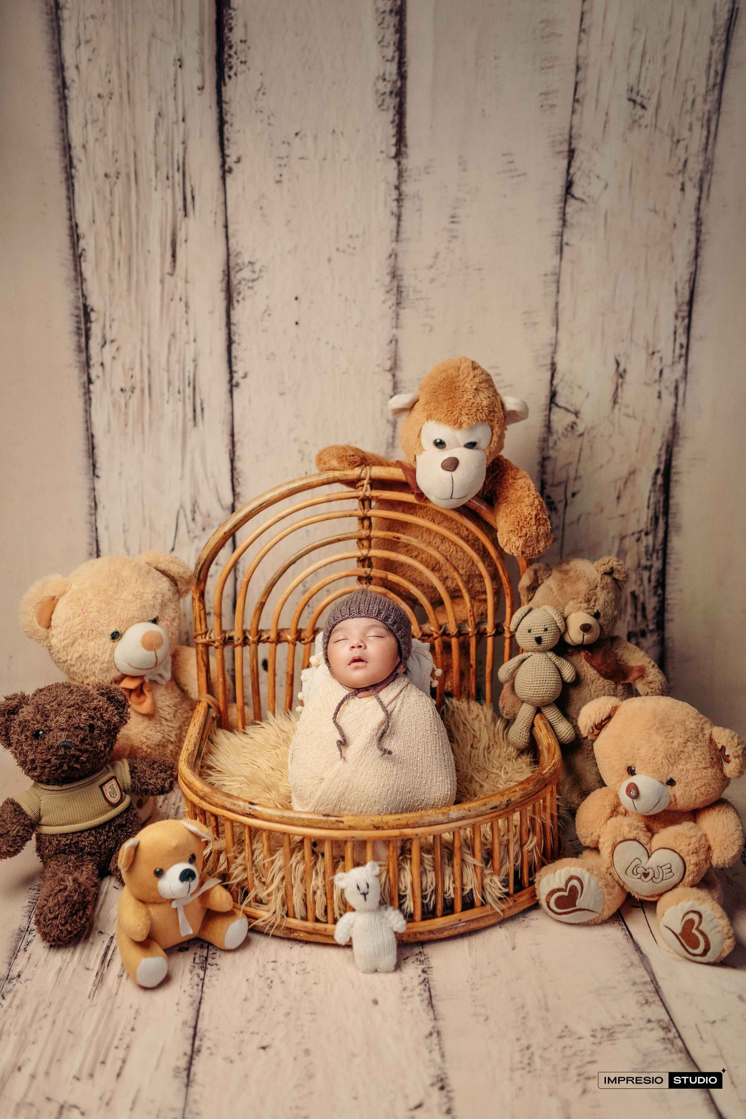 Newborn baby sleeping in wicker basket surrounded by teddy bears on white wood backdrop.