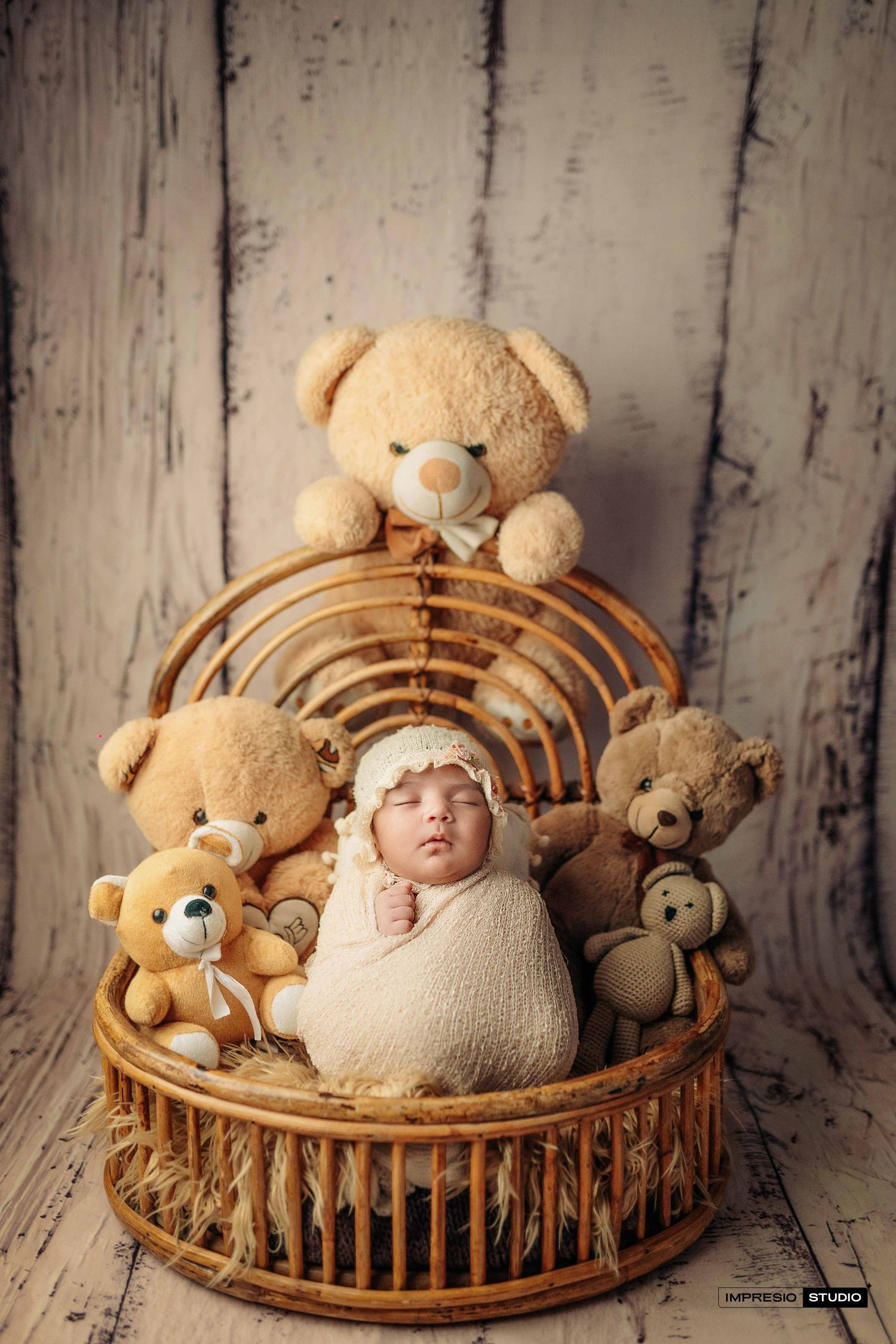 Newborn baby wrapped in cream swaddle sleeping in wicker basket surrounded by soft teddy bears.