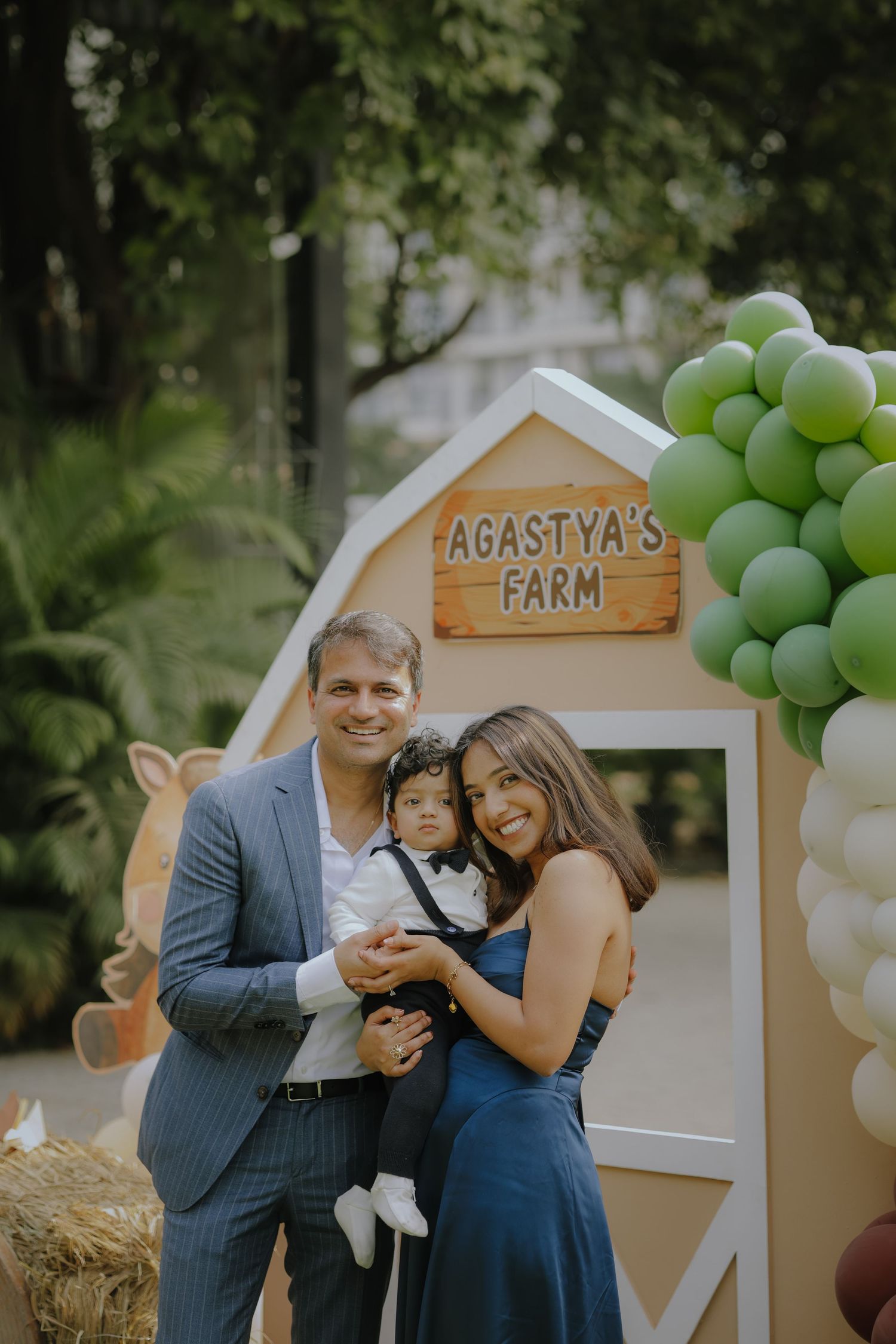 Family posing at Agastya's Farm themed birthday party with green balloon decorations and barn backdrop.