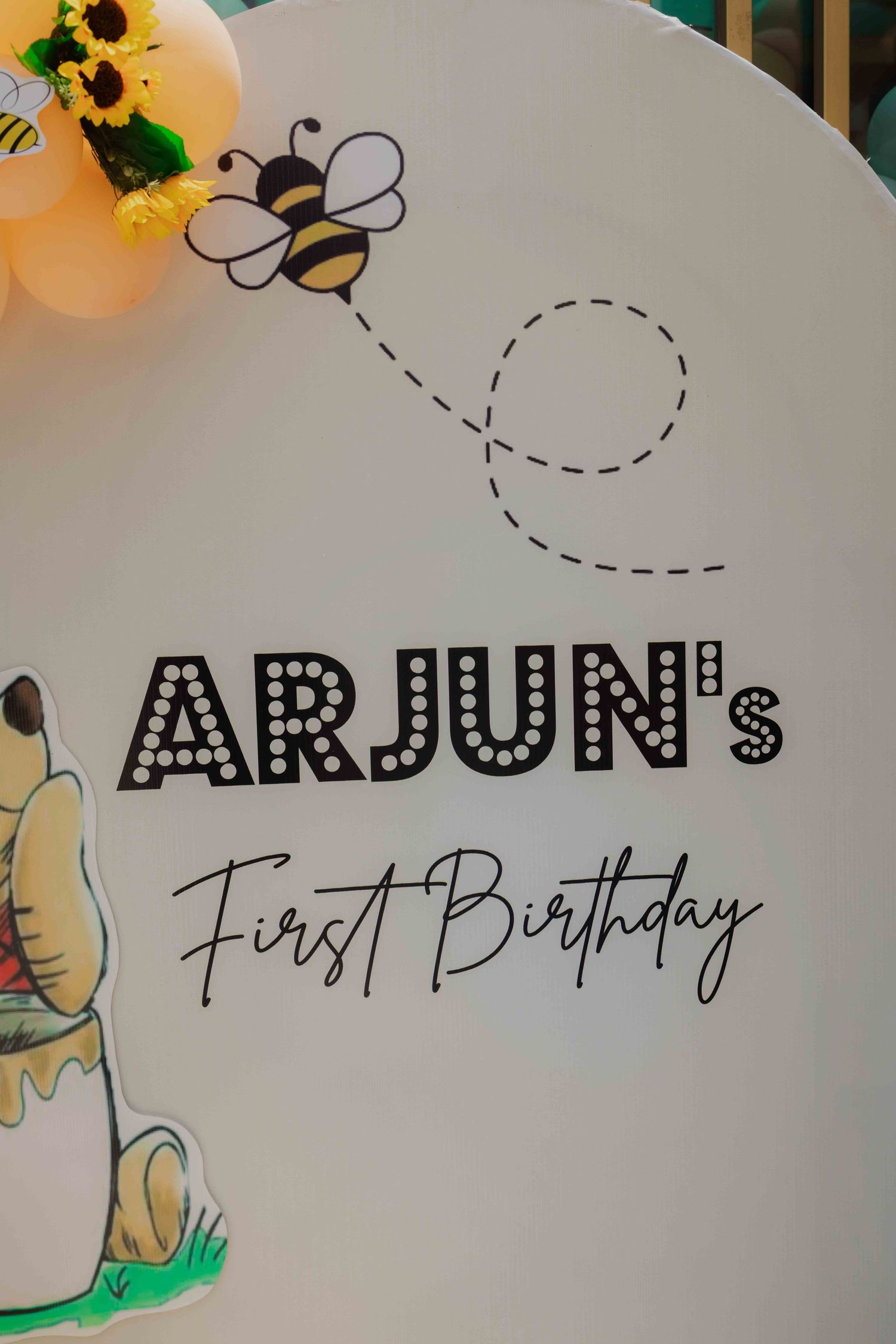 Arjun's First Birthday party backdrop with Winnie the Pooh, a bee, sunflowers, and pastel balloons.