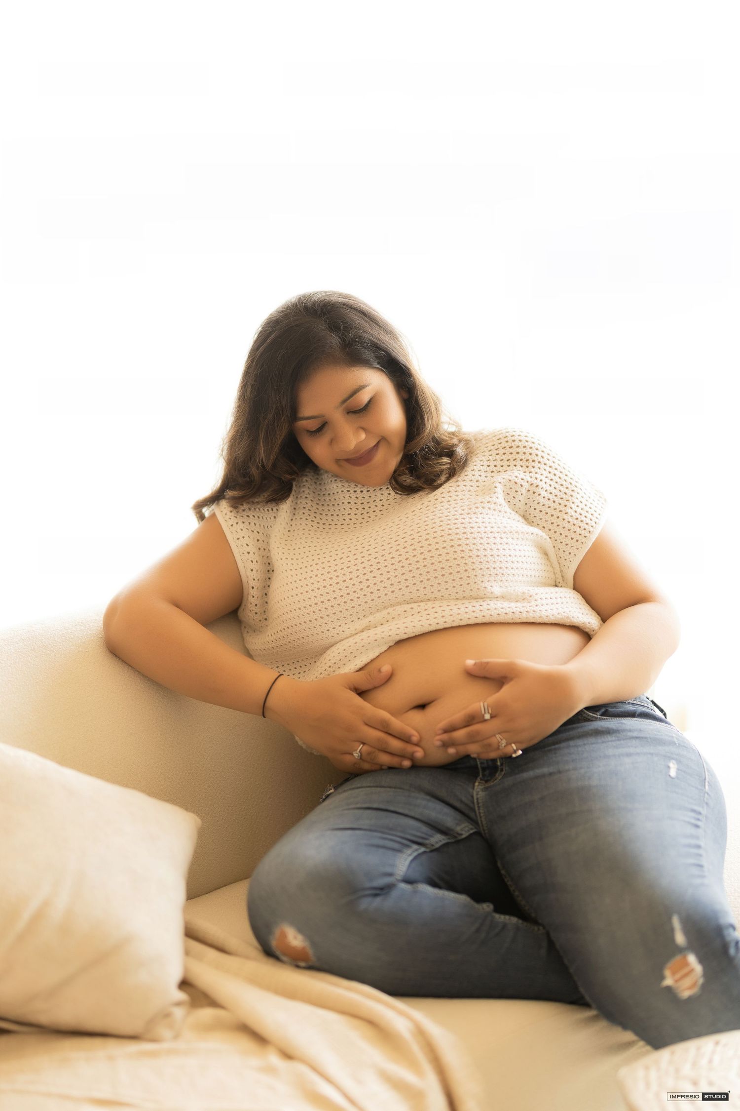 Side view sequence of a pregnant woman in jeans and sweater relaxing on white bedding.