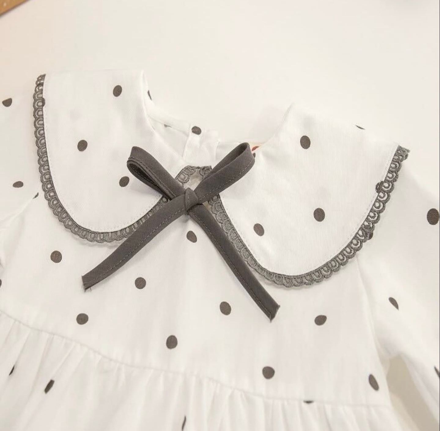 Close-up of a white polka dot blouse with a black bow and lace trim detail on the Peter Pan collar.