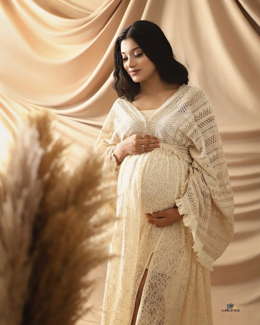 Maternity portrait in cream knit dress with soft fabric backdrop and pampas grass.