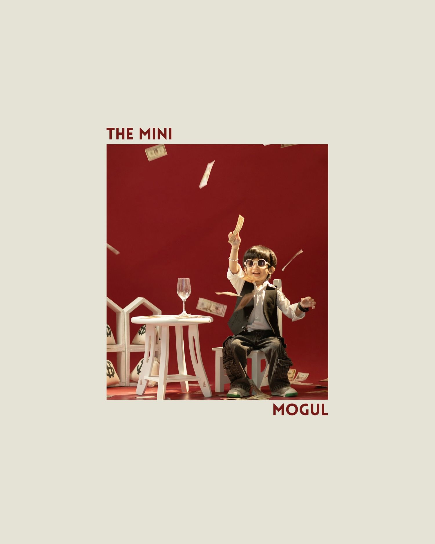 A small boy figurine tosses money in the air beside a white table, titled The Mini Mogul on a red background.