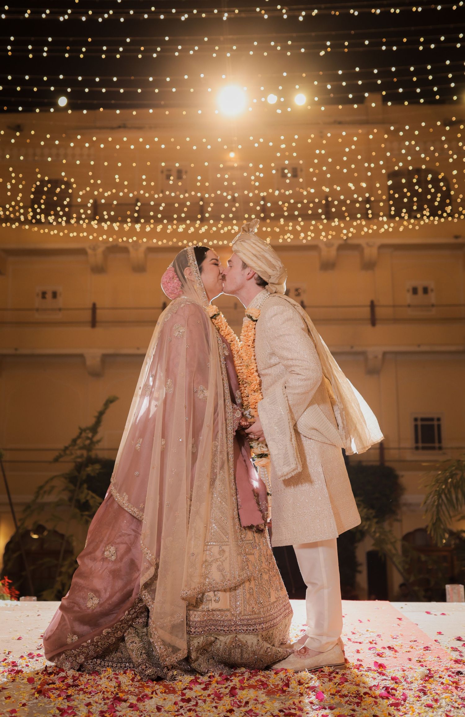 A romantic wedding scene with string lights overhead and rose petals scattered on the dance floor.